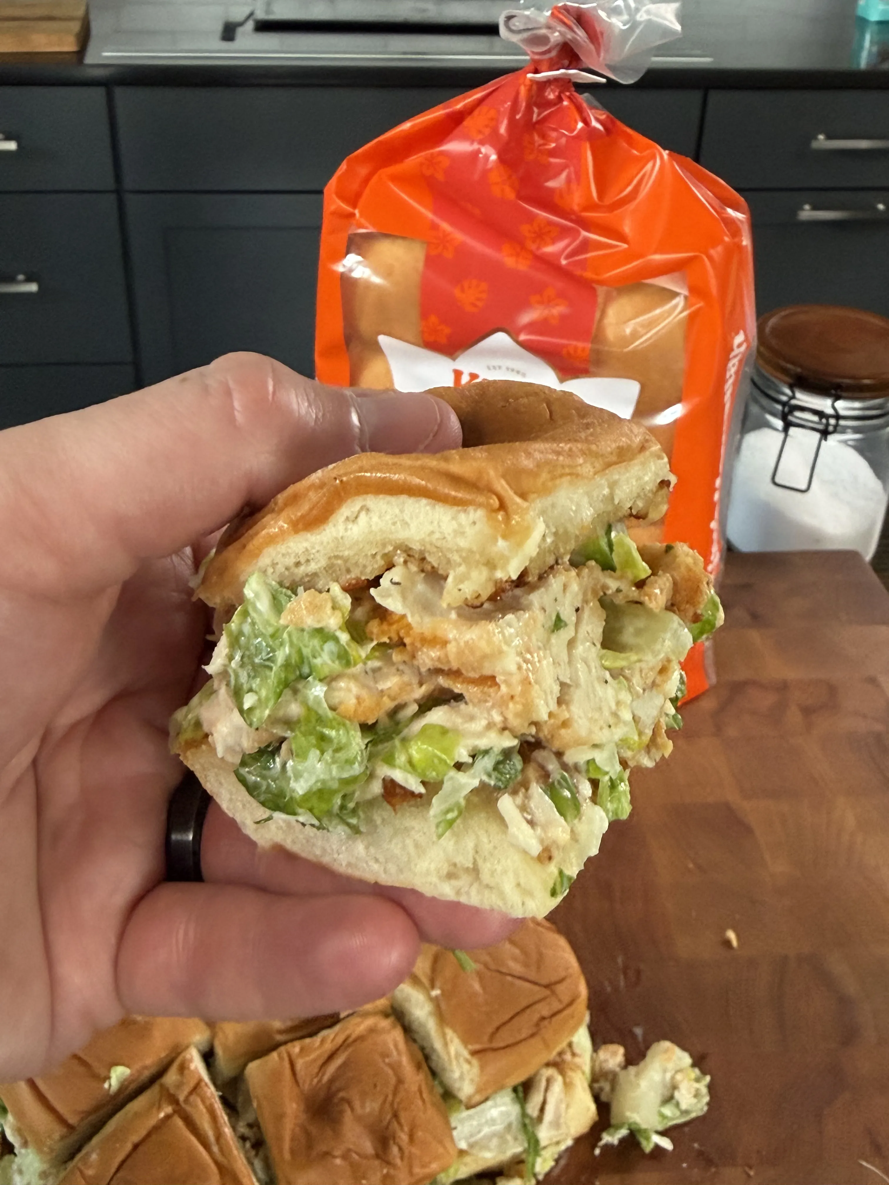 Hand holding a crispy chicken caesar slider on a Hawaiian roll