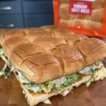 Chicken caesar salad sliders made with King's Hawaiian sweet rolls, filled with lettuce and dressing on cutting board