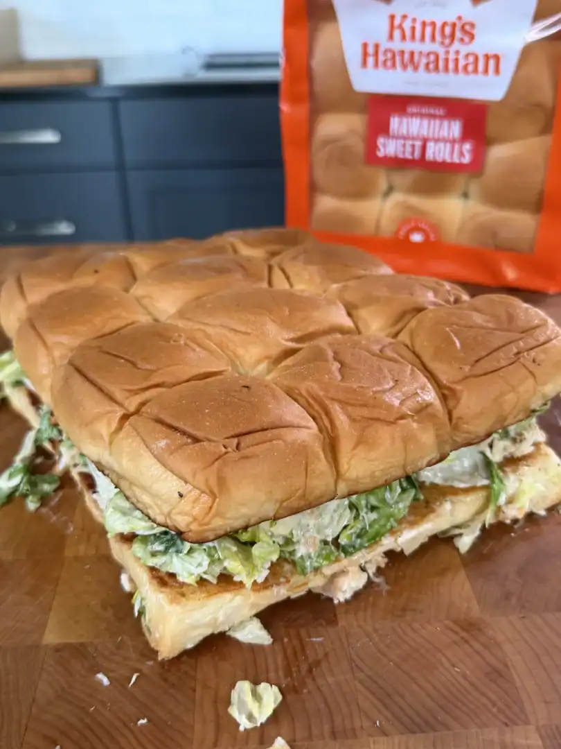 Chicken caesar salad sliders made with King's Hawaiian sweet rolls, filled with lettuce and dressing on cutting board