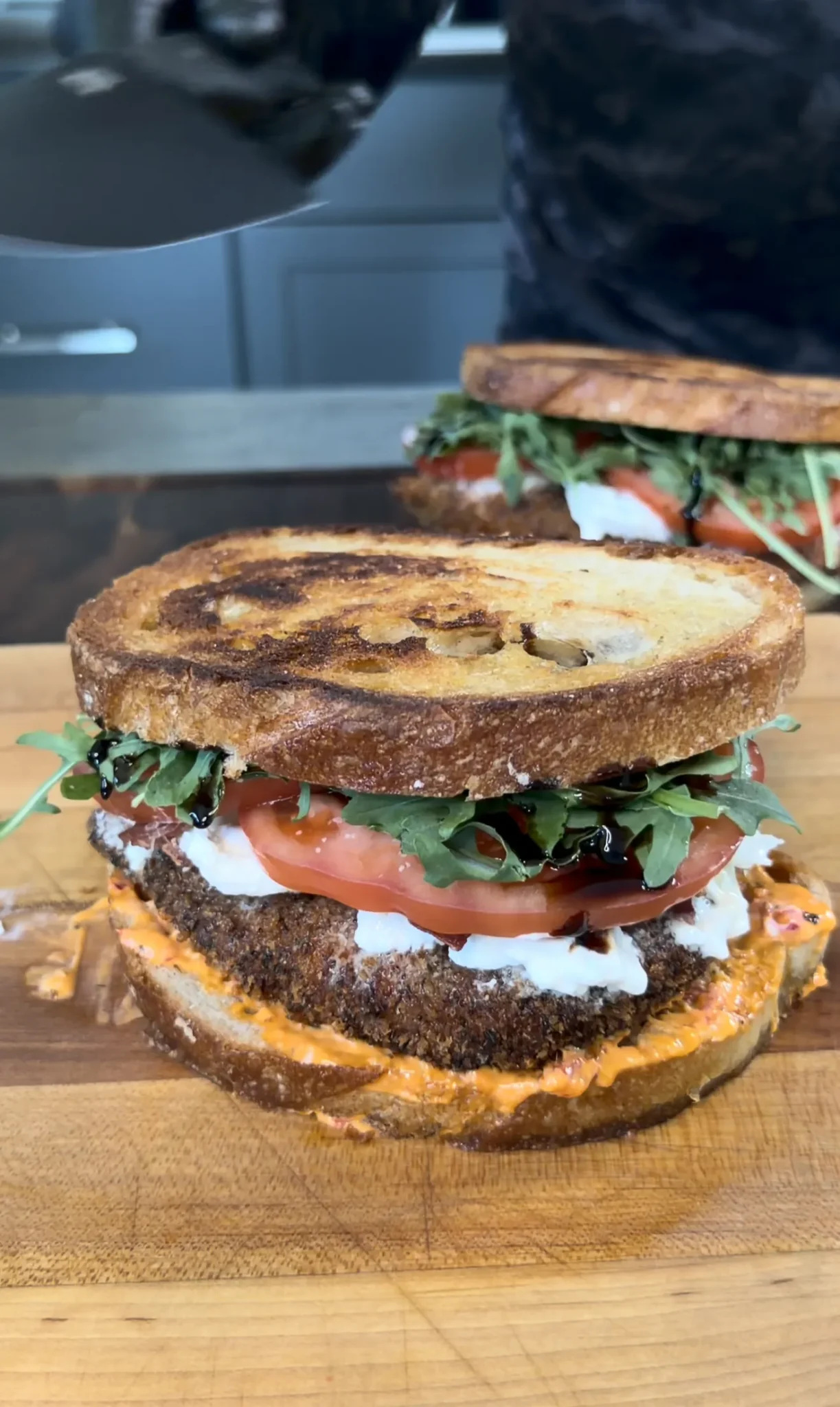 Crispy chicken cutlet sandwich on marble rye bread with tomatoes, arugula and spread on wooden cutting board