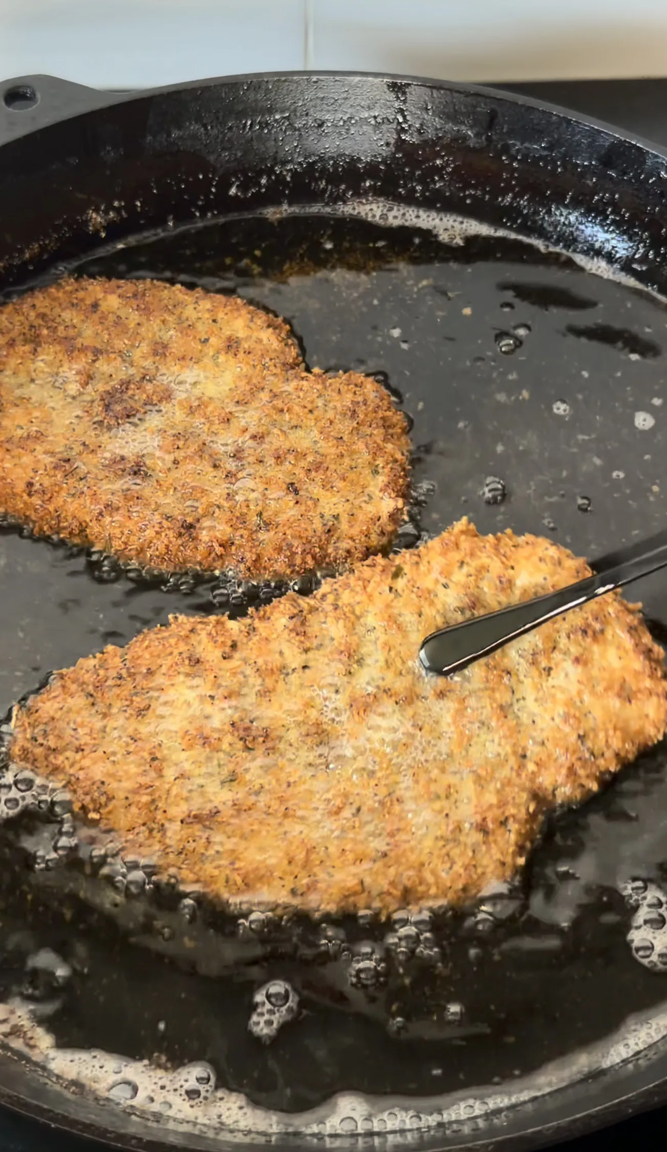 Crispy chicken cutlets frying in a cast iron skillet