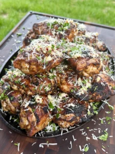 Golden brown garlic parmesan chicken thighs in cast iron skillet topped with melted cheese and fresh herbs