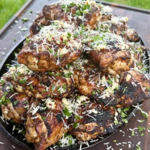 Golden brown garlic parmesan chicken thighs in cast iron skillet topped with melted cheese and fresh herbs
