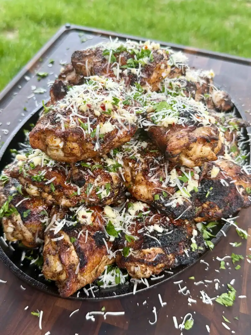 Golden brown garlic parmesan chicken thighs in cast iron skillet topped with melted cheese and fresh herbs