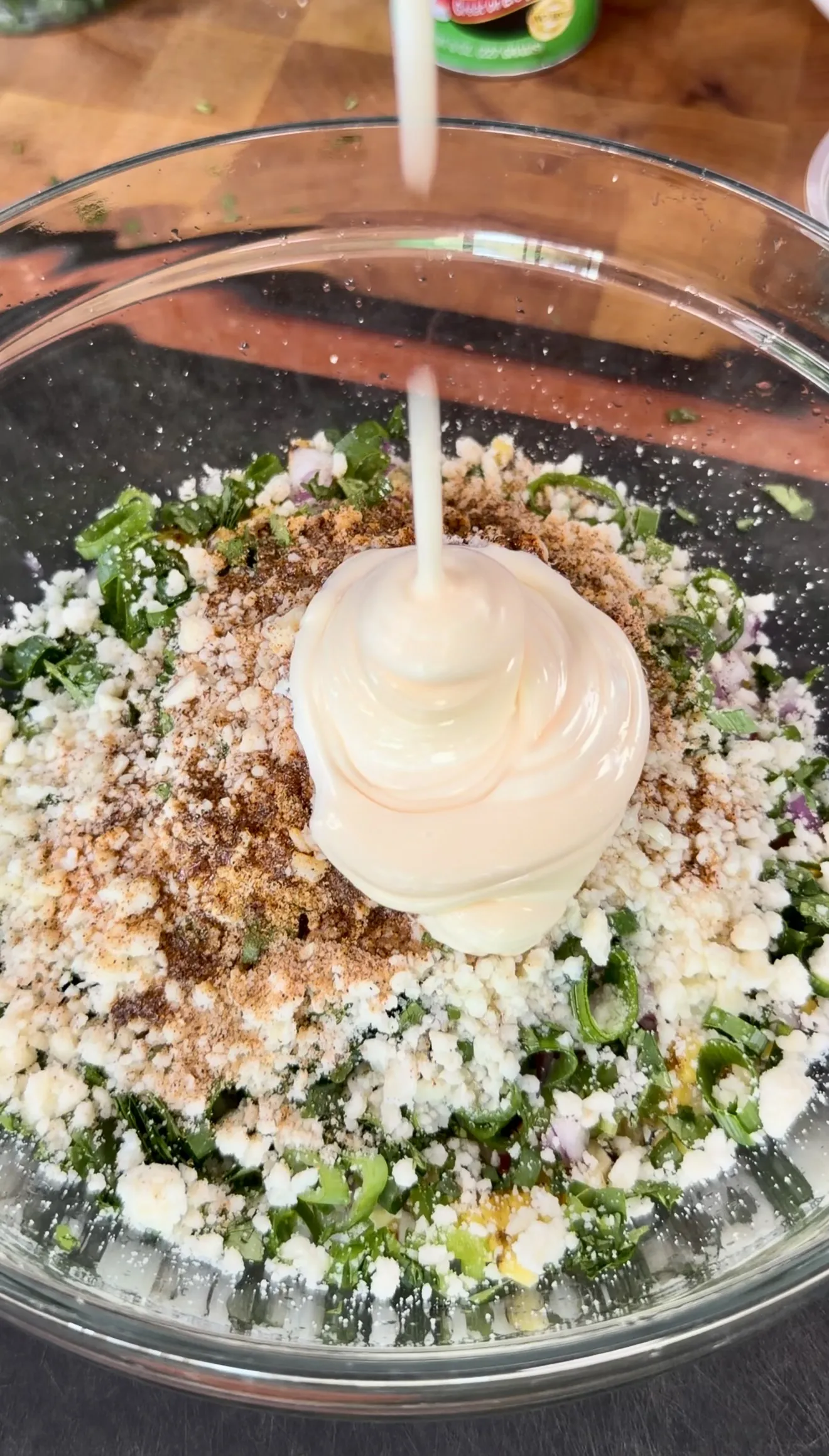 Mexican street corn elote being mixed in a glass bowl with cotija cheese, herbs, and spices