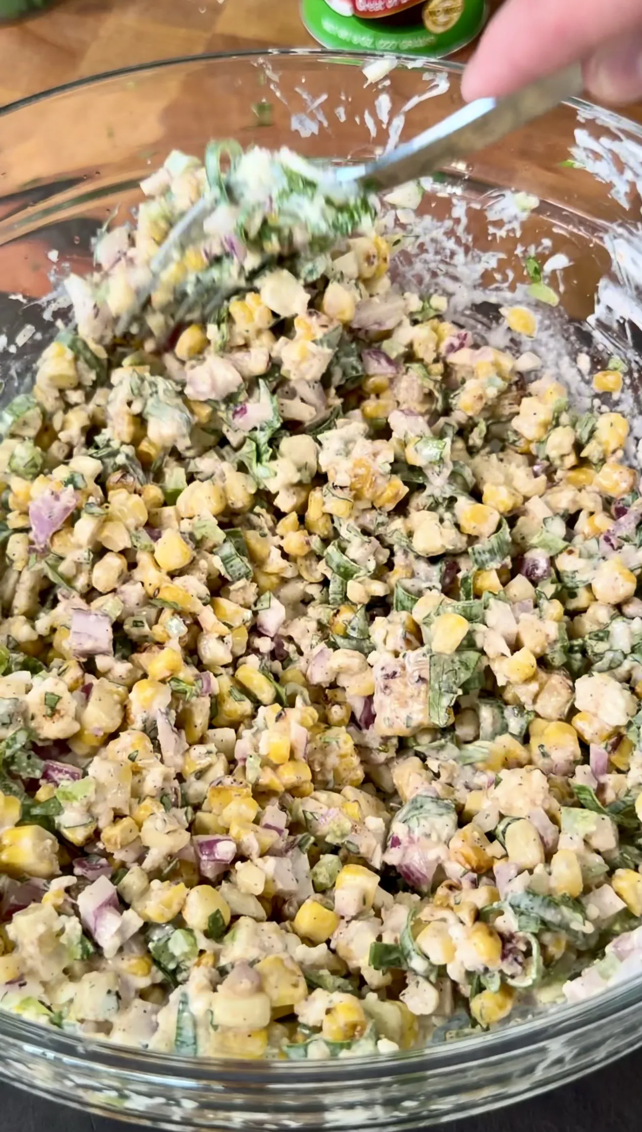 Fresh creamy elote corn salad with diced vegetables and herbs mixed in a glass bowl