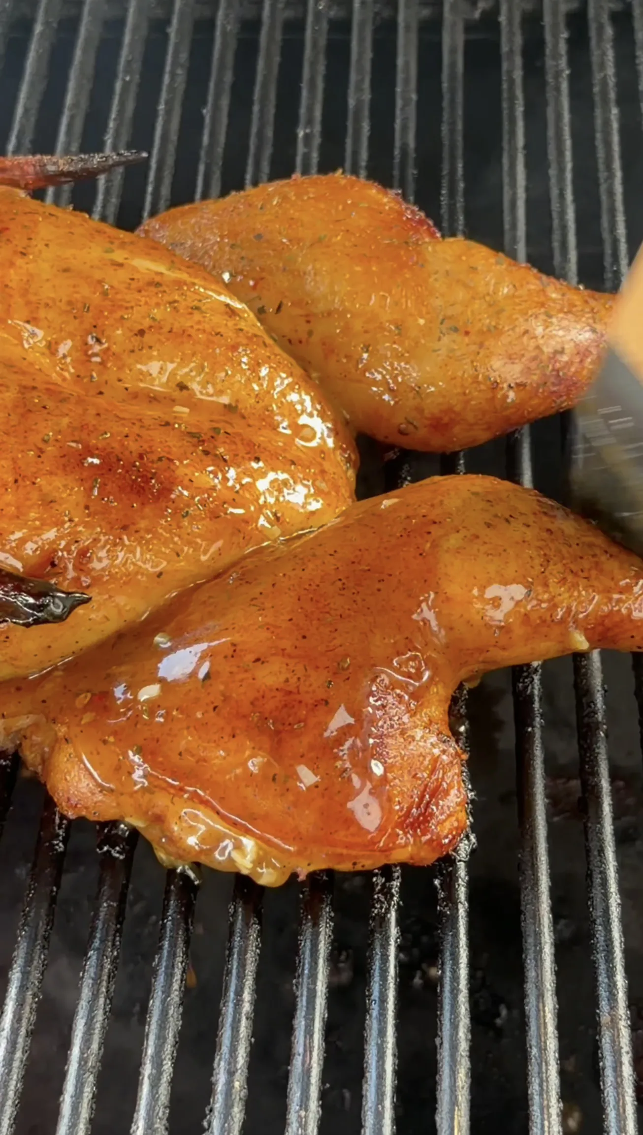 Glazed spatchcock chicken grilling on grates with caramelized skin