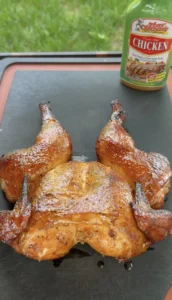 Golden brown spatchcock smoked chicken with crispy skin on a dark cutting board with seasoning jar