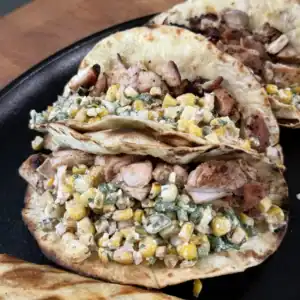 Grilled chicken elote tacos with corn salsa and cilantro served on flour tortillas in a black cast iron skillet