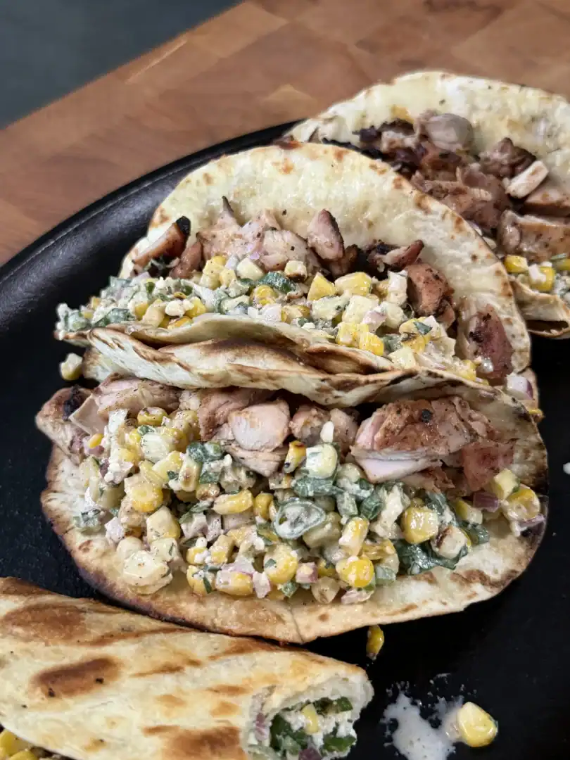 Grilled chicken elote tacos with corn salsa and cilantro served on flour tortillas in a black cast iron skillet