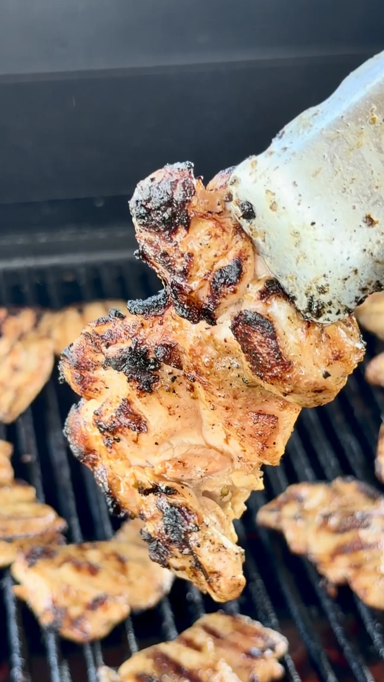 Charred grilled chicken being lifted from the barbecue with tongs for elote tacos