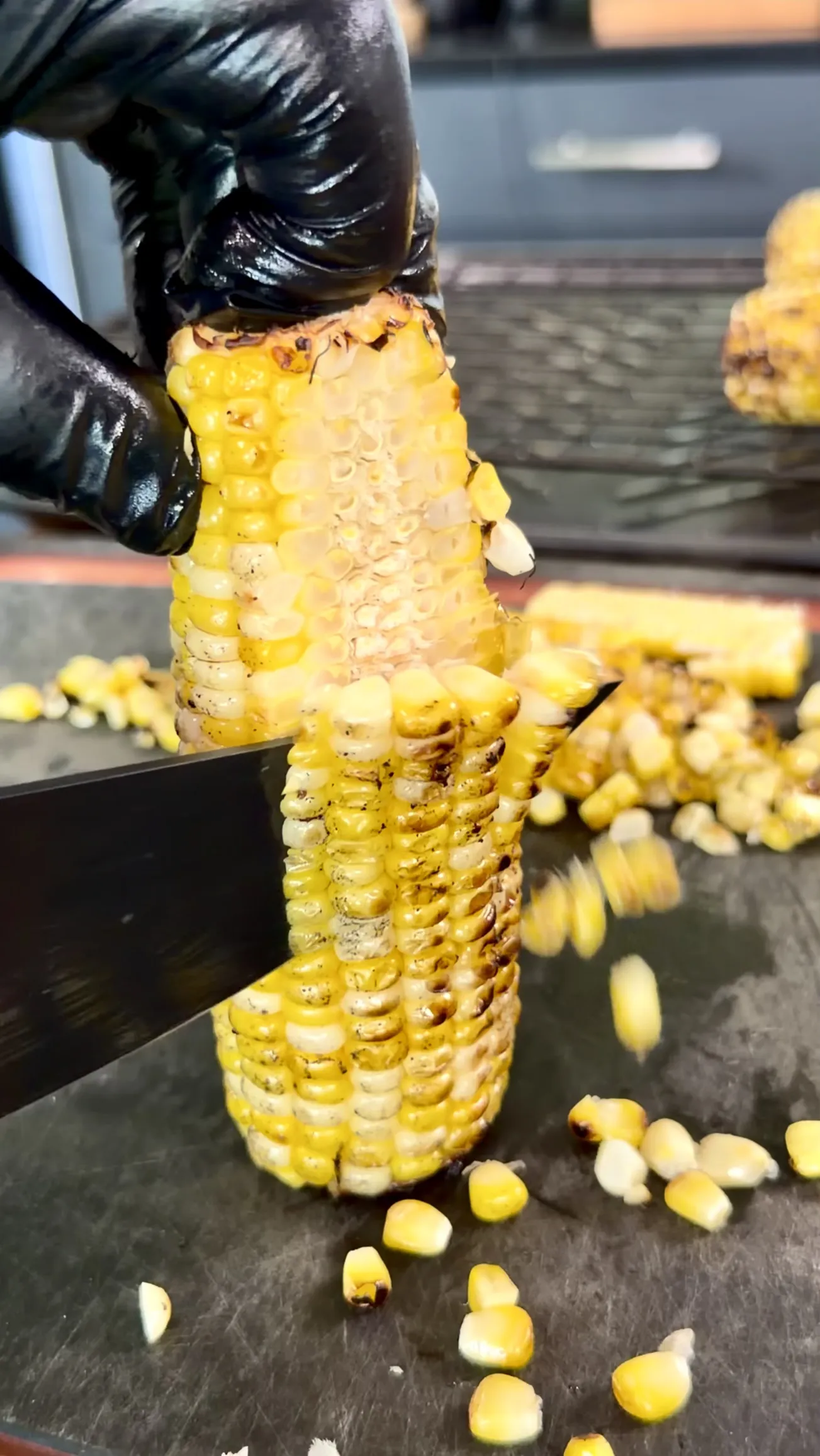 Hands in black gloves removing kernels from a grilled corn cob