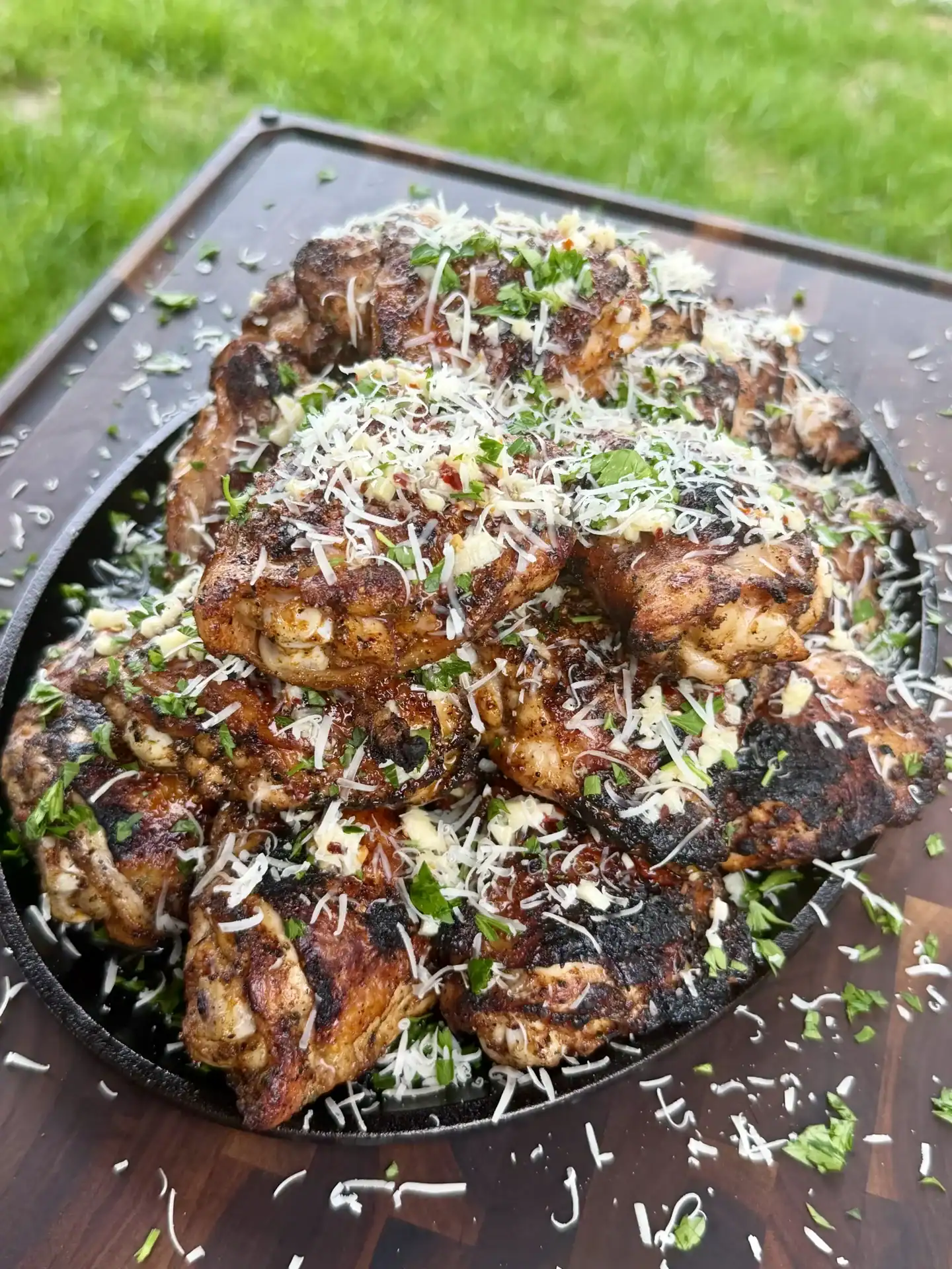 Golden-brown grilled garlic parmesan chicken thighs in cast iron skillet topped with melted cheese and fresh herbs