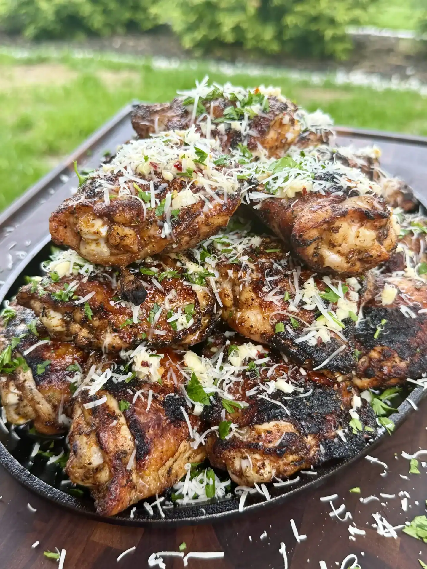 Golden-brown grilled garlic parmesan chicken thighs in cast iron skillet topped with fresh herbs and grated cheese
