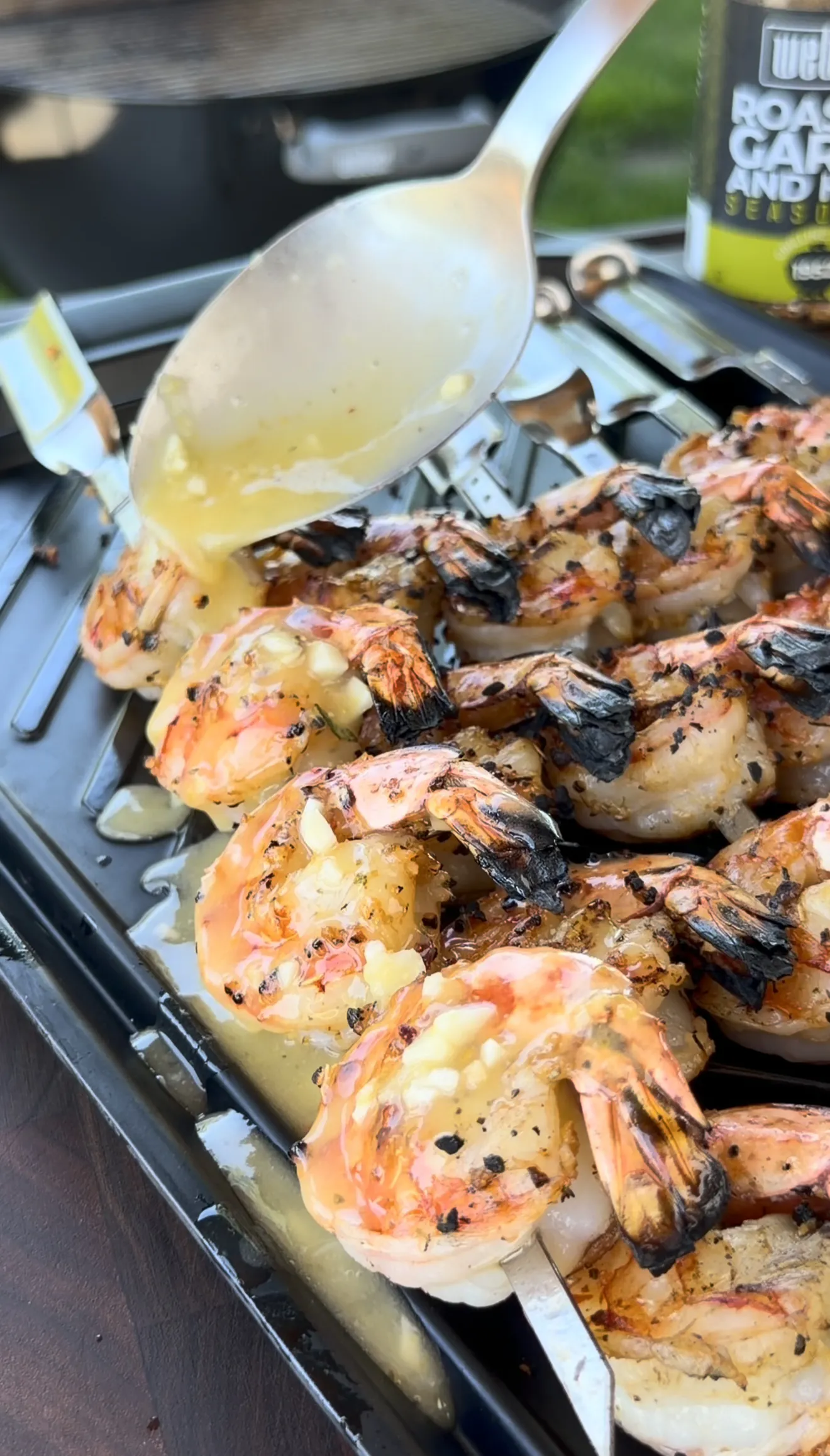 Grilled shrimp skewers being basted with melted garlic herb butter on the grill
