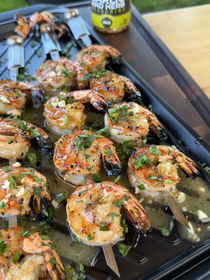 Grilled shrimp skewers with fresh herbs on a black serving tray, golden brown and ready to serve
