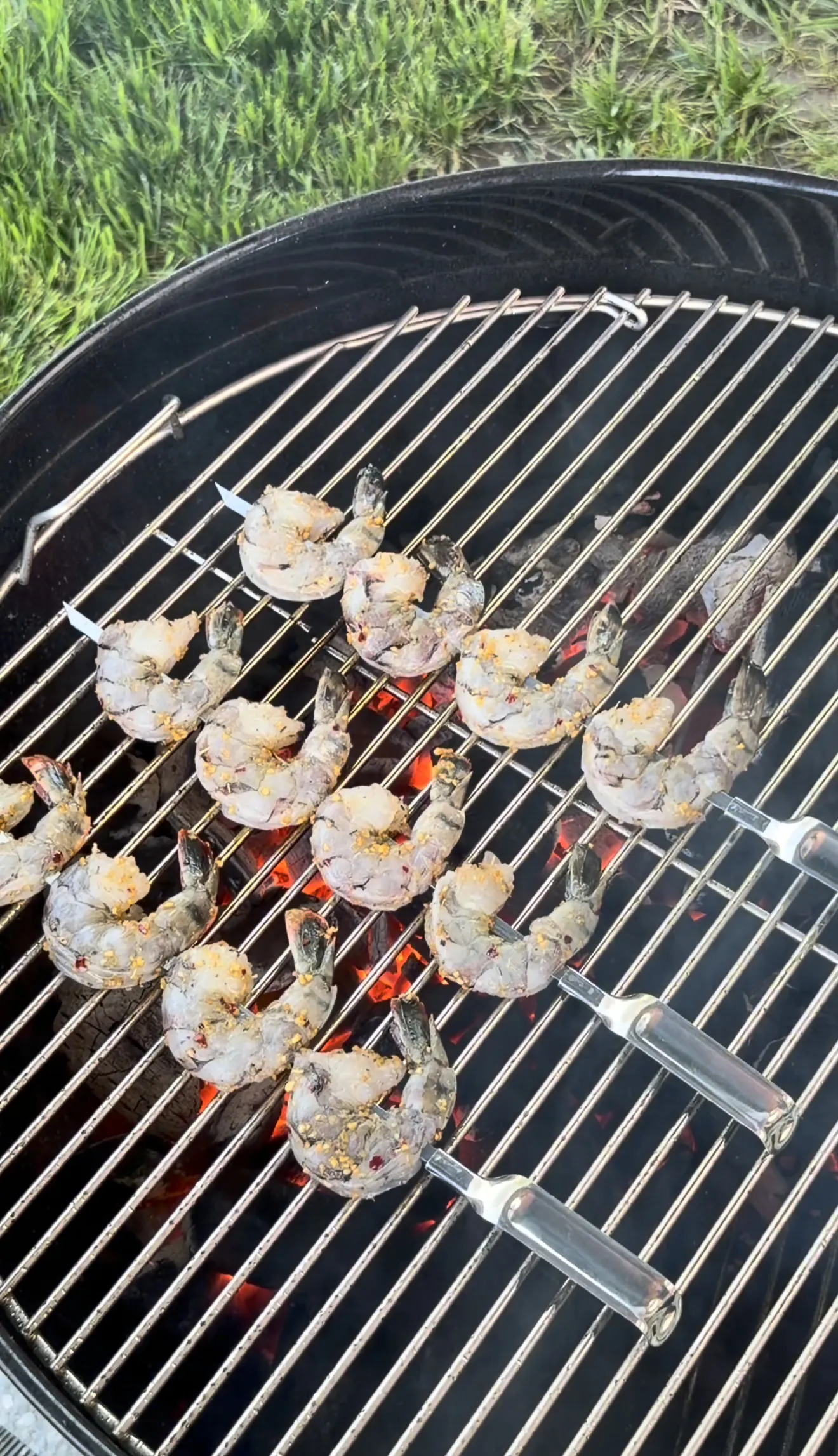 Garlic herb grilled shrimp skewers cooking on a round barbecue grill with visible flames
