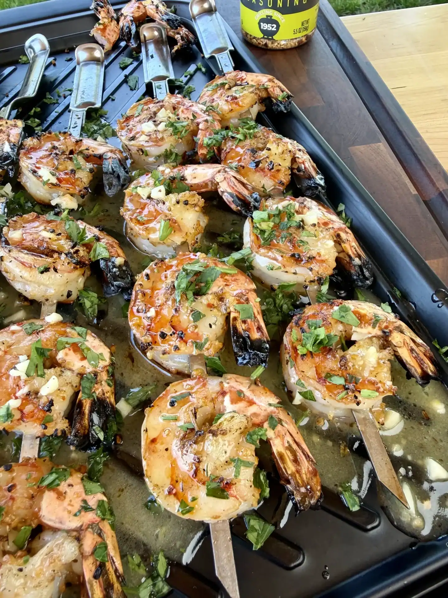 Grilled shrimp skewers with herbs on a black grill pan, garnished with fresh parsley and garlic