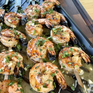 Grilled shrimp skewers with herbs on a black grill pan, garnished with fresh parsley and garlic