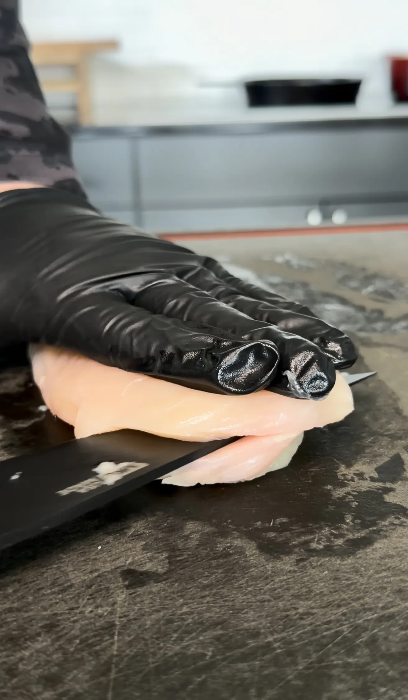 Hands preparing chicken cutlet wearing black gloves