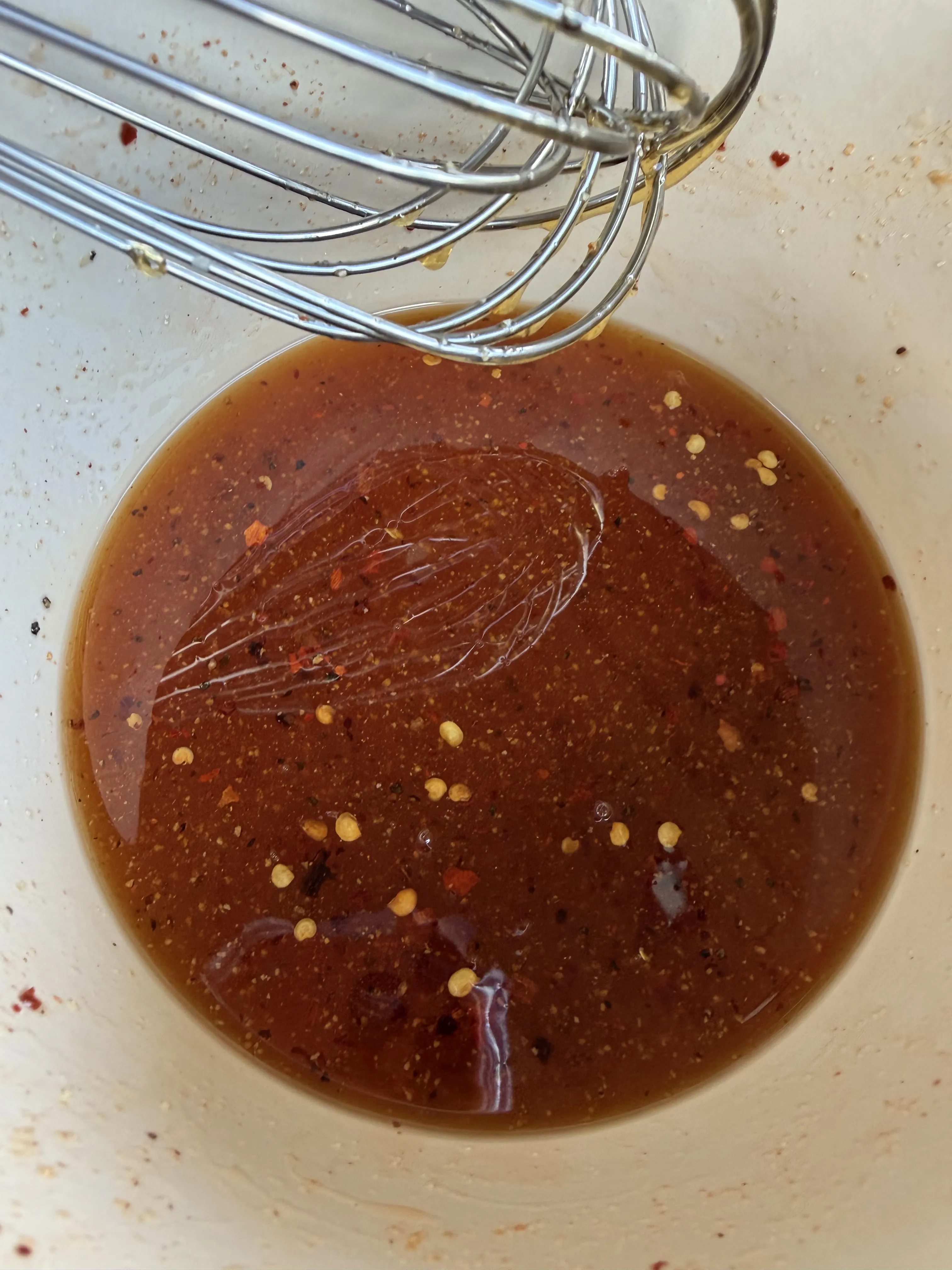Dark amber hot honey glaze with spices in a white bowl with whisk