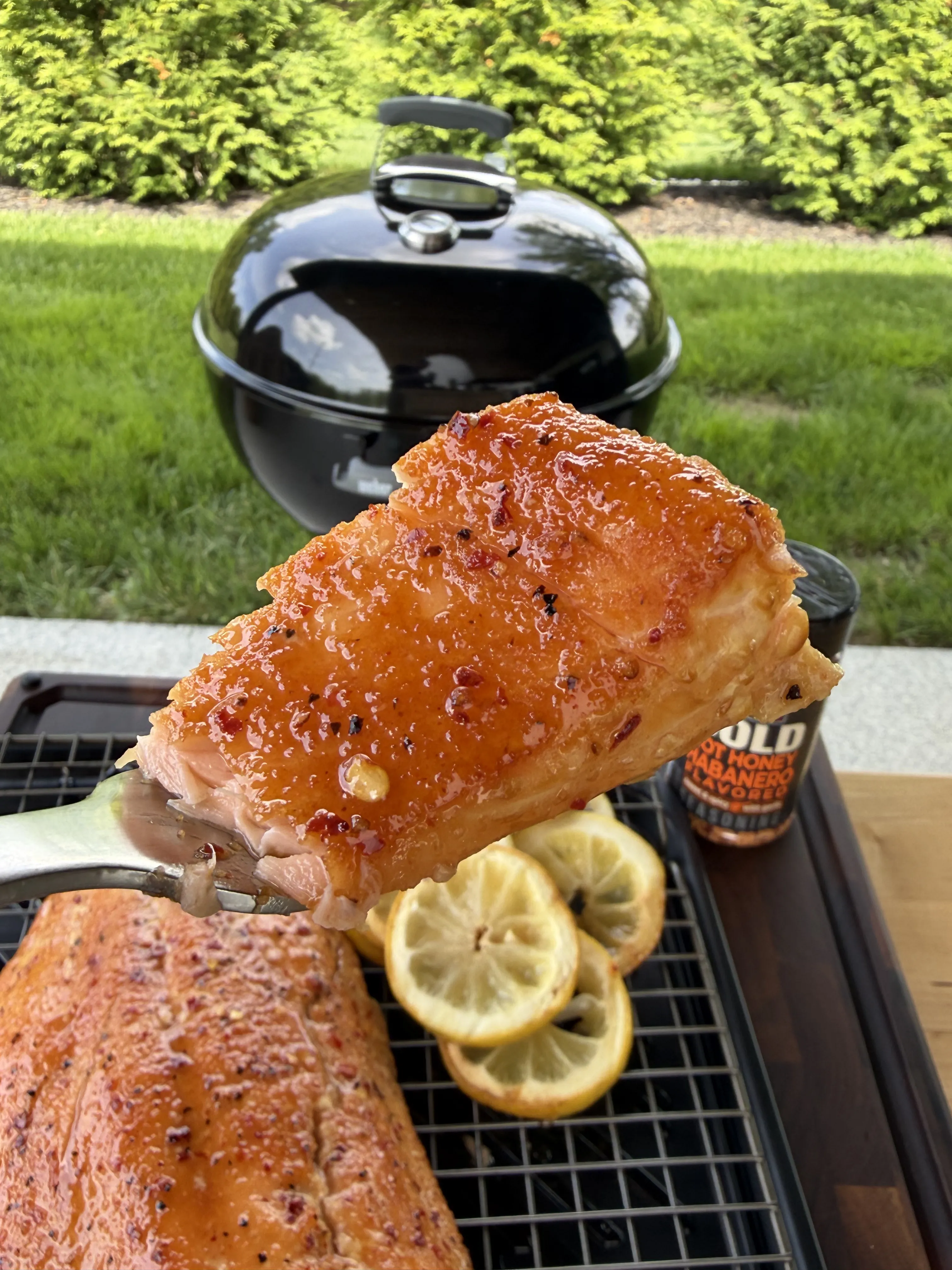 Hot honey glazed smoked salmon on grill grates with lemon slices and Weber kettle in background