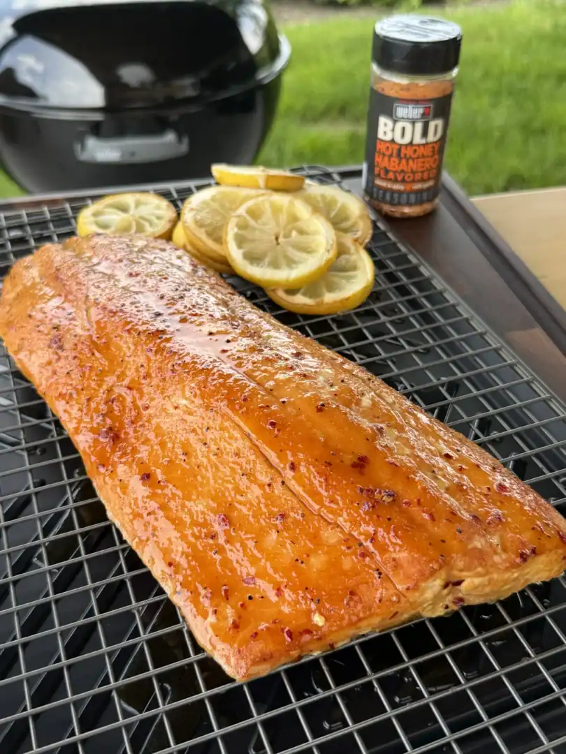 Hot honey glazed smoked salmon fillet on cooling rack with lemon slices and Weber BOLD seasoning bottle