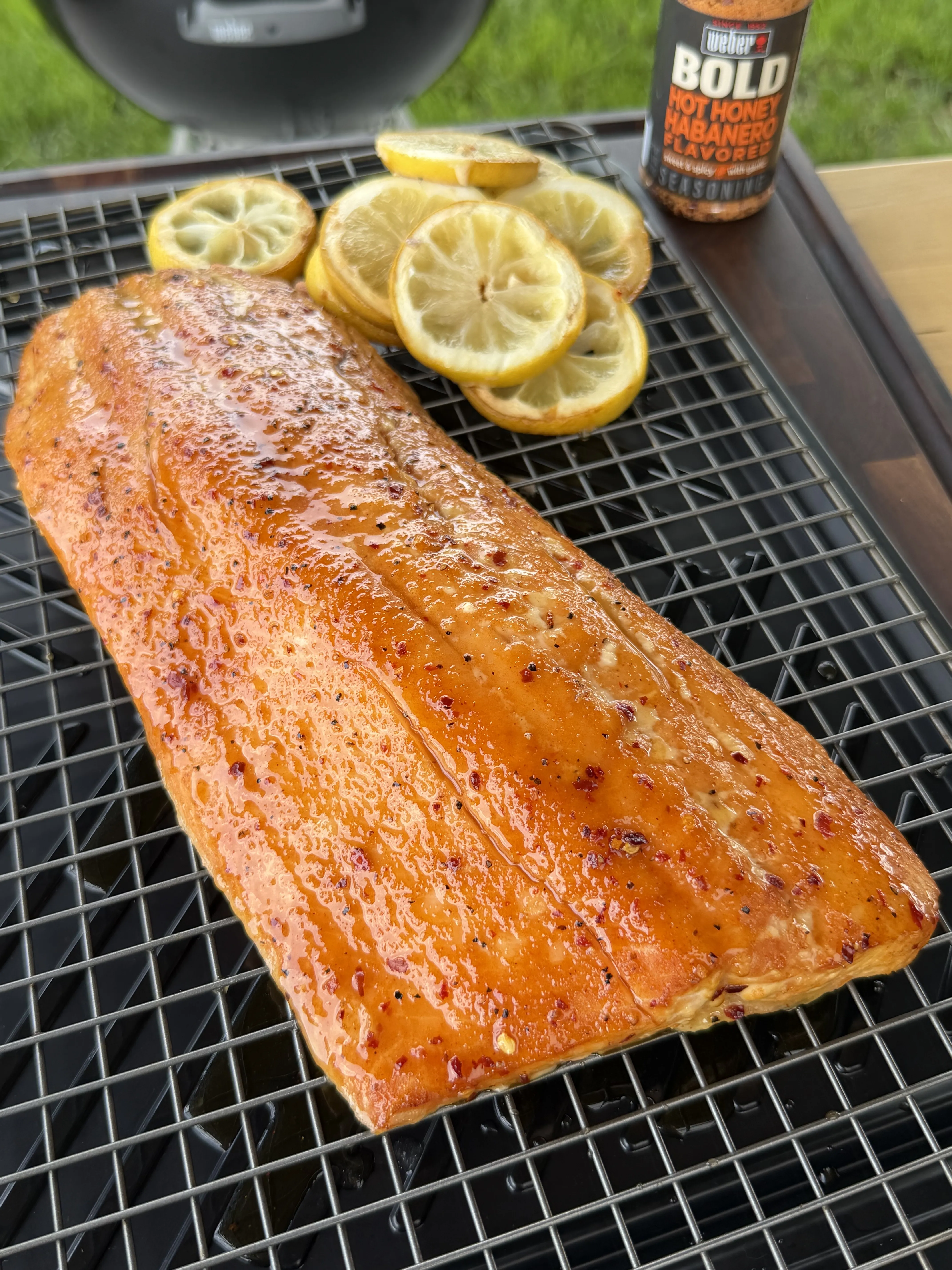 Golden glazed hot honey smoked salmon fillet on grill grates with lemon slices