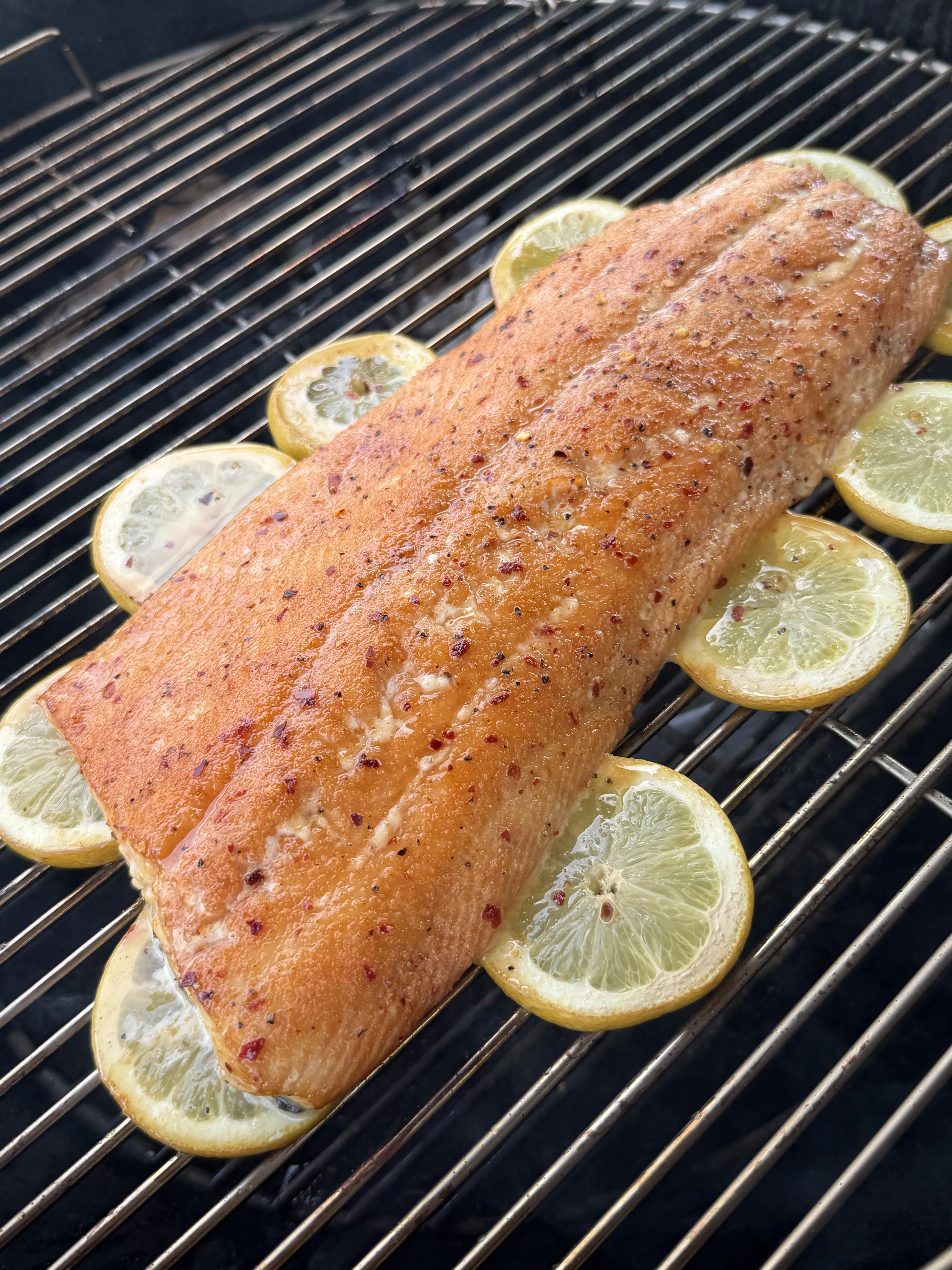 Hot honey smoked salmon fillet smoking on grill grates with lemon slices underneath