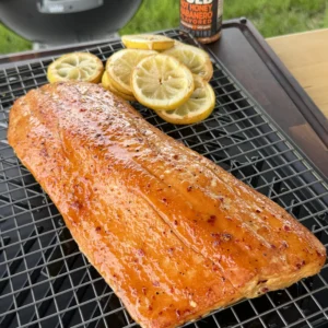 Golden glazed hot honey smoked salmon fillet on grill grate with lemon slices and spice bottle