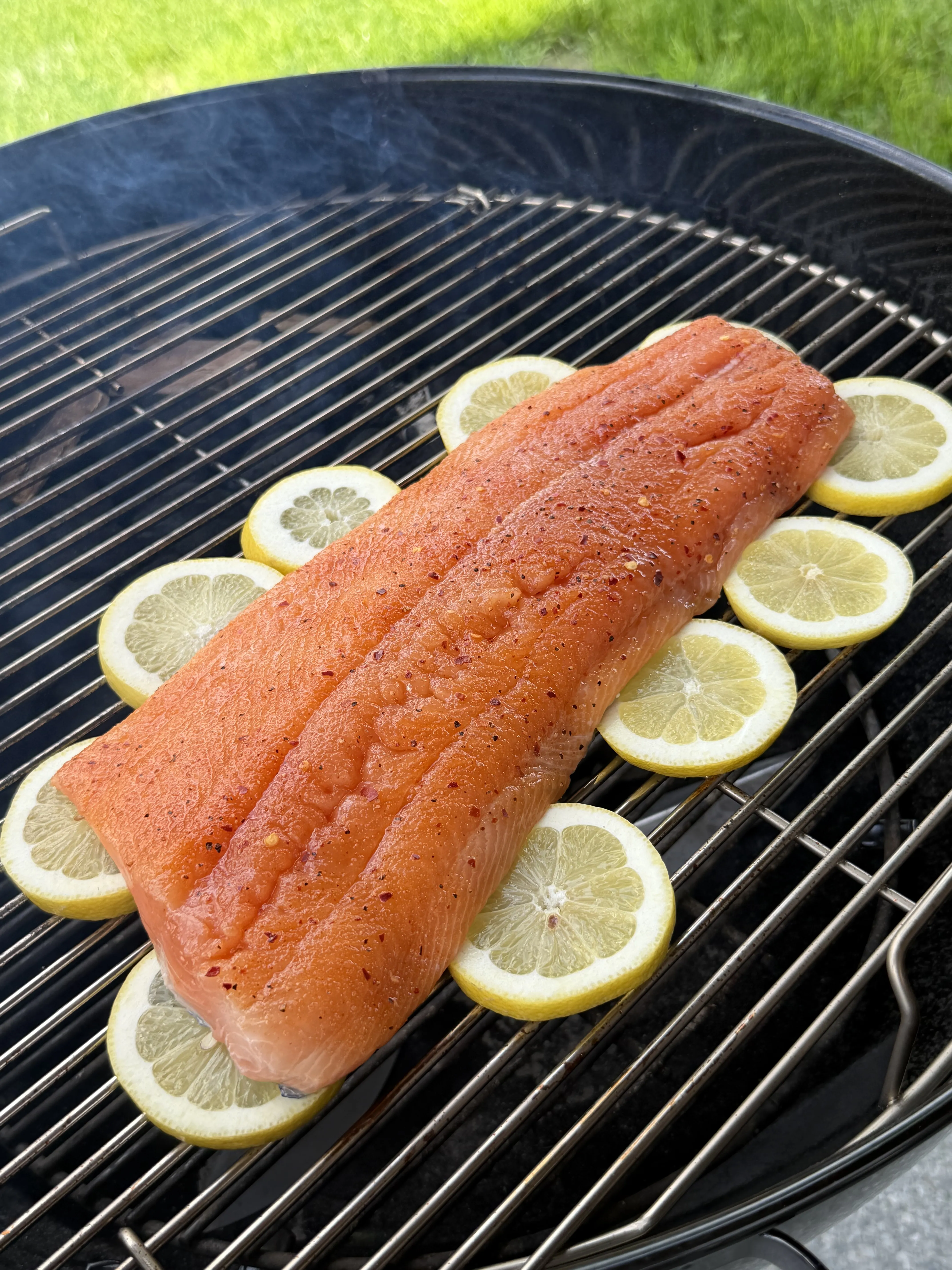 Hot honey smoked salmon fillet seasoned and grilling on barbecue grates with fresh lemon slices