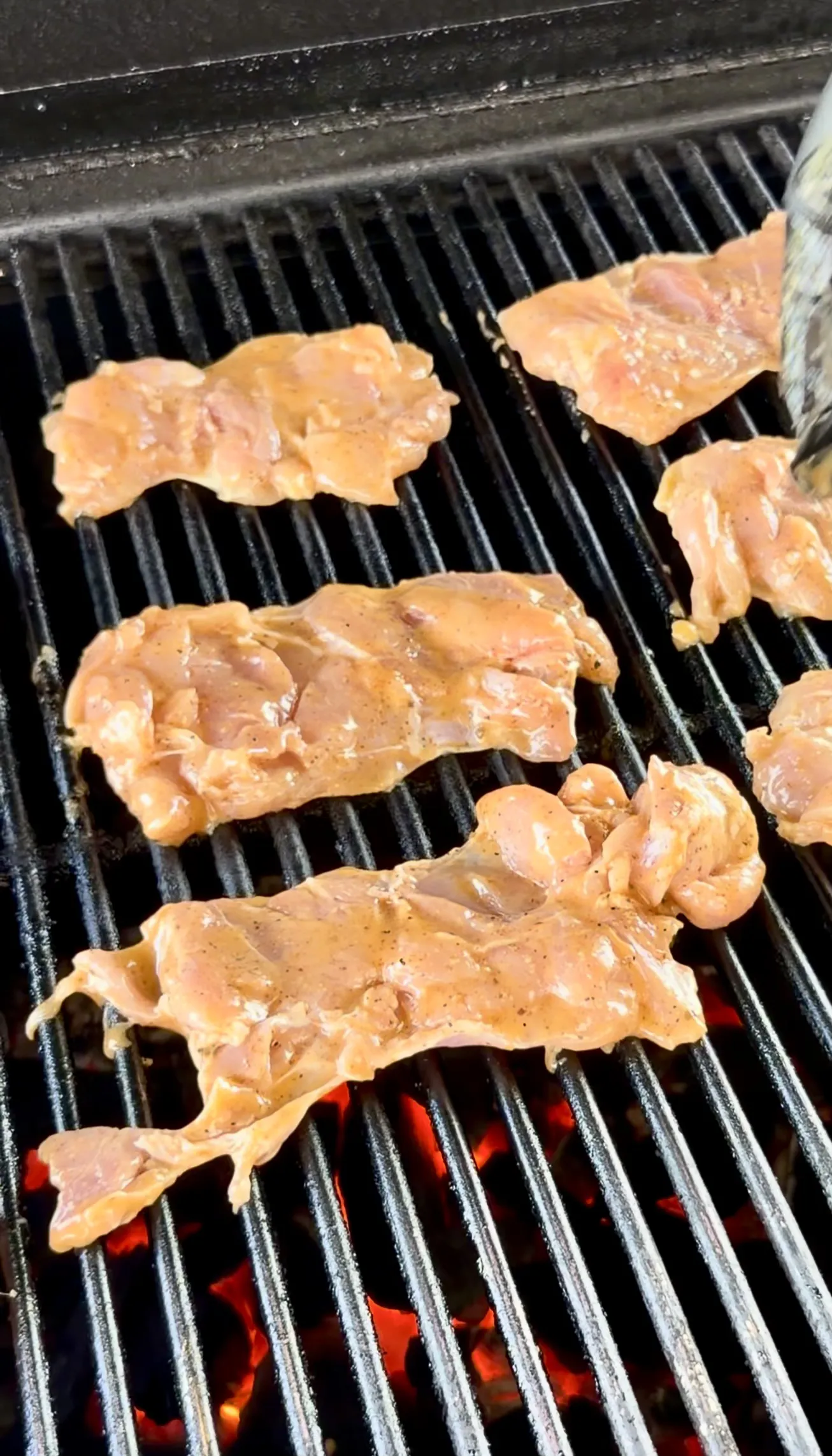 Marinated chicken thighs cooking on grill grates over glowing coals for elote tacos