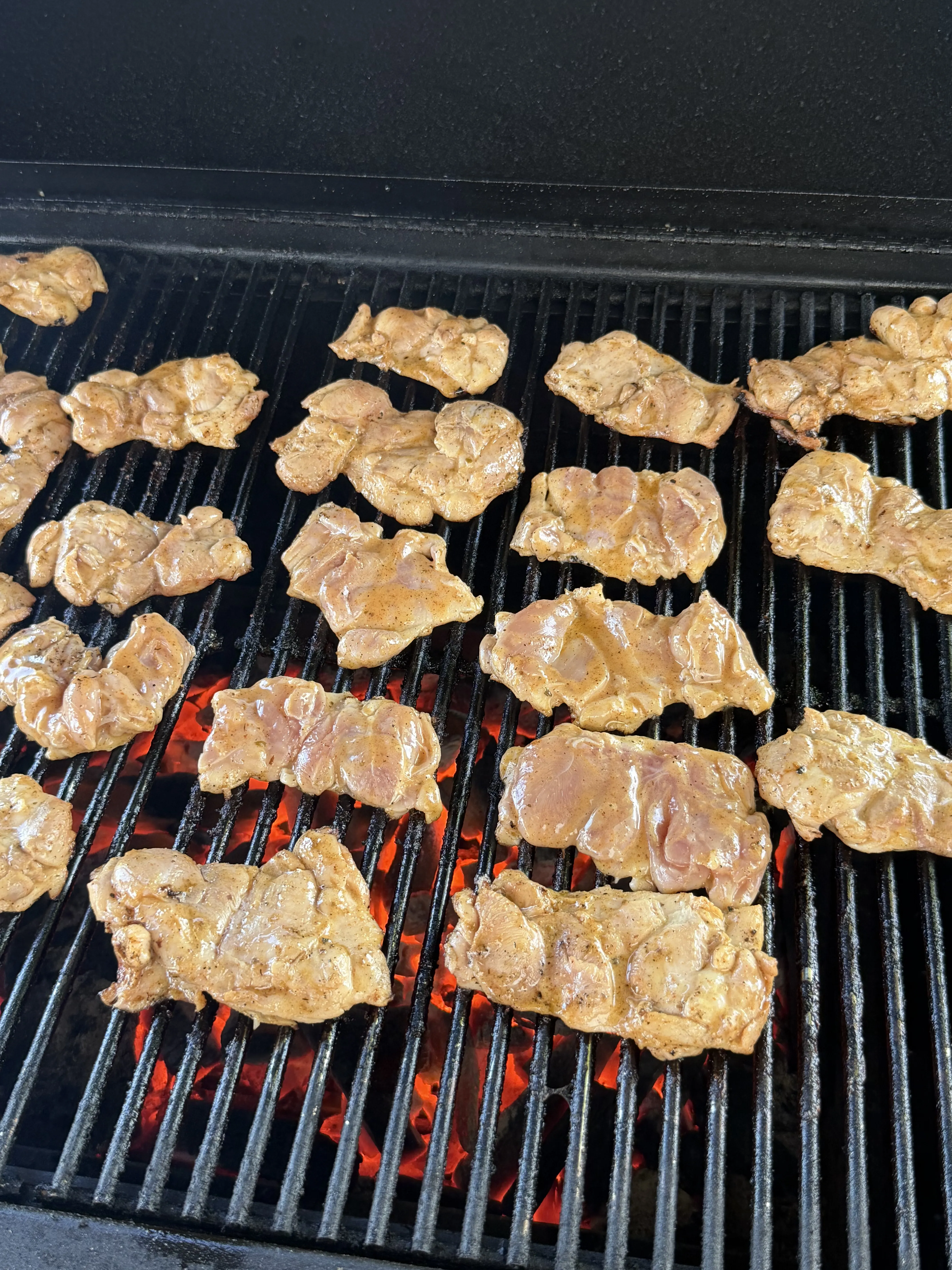 Marinated chicken thighs cooking on a charcoal grill with visible grill marks and red hot coals