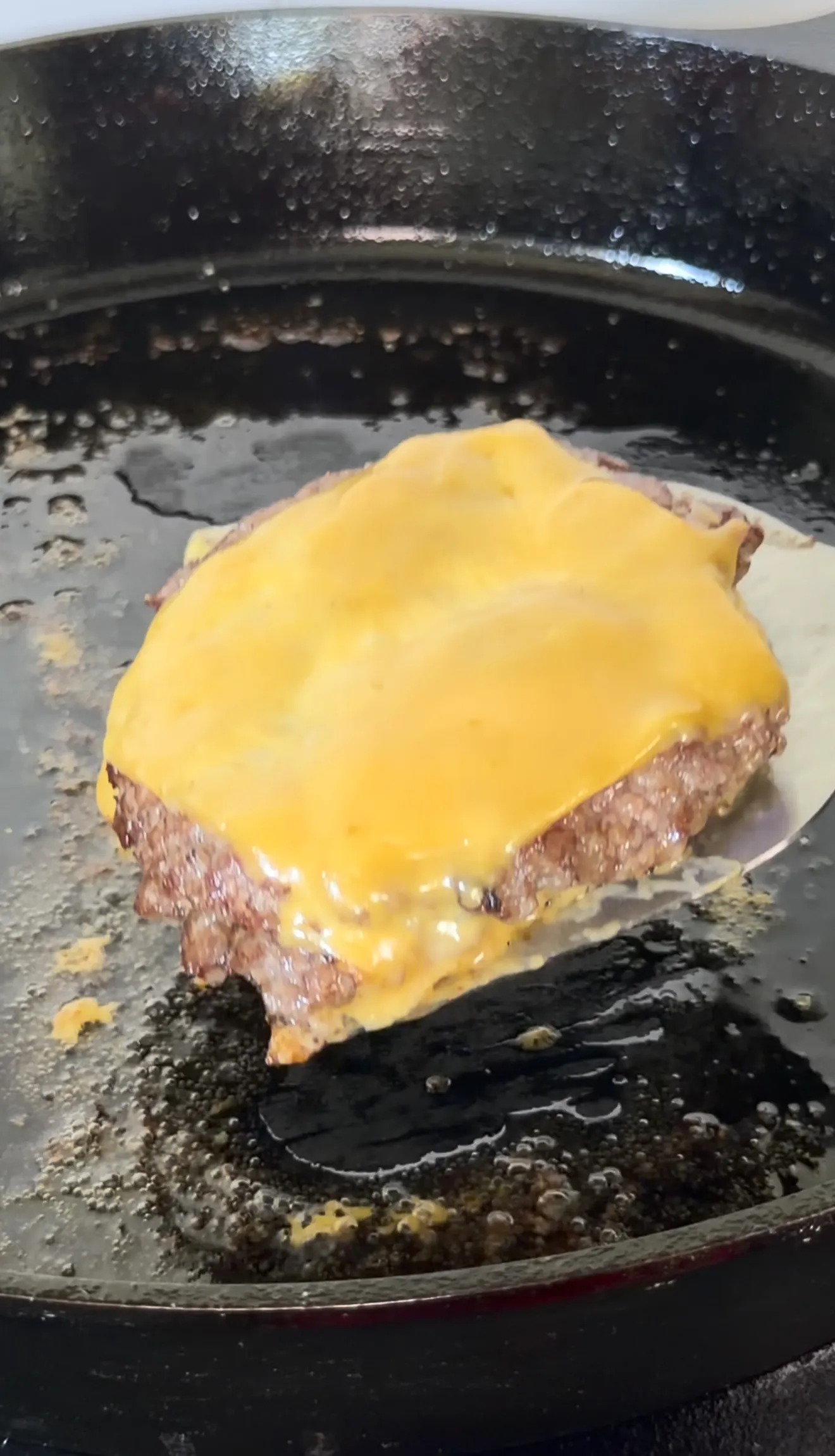 Bacon jam smash burger with melted cheese cooking on a griddle with spatula