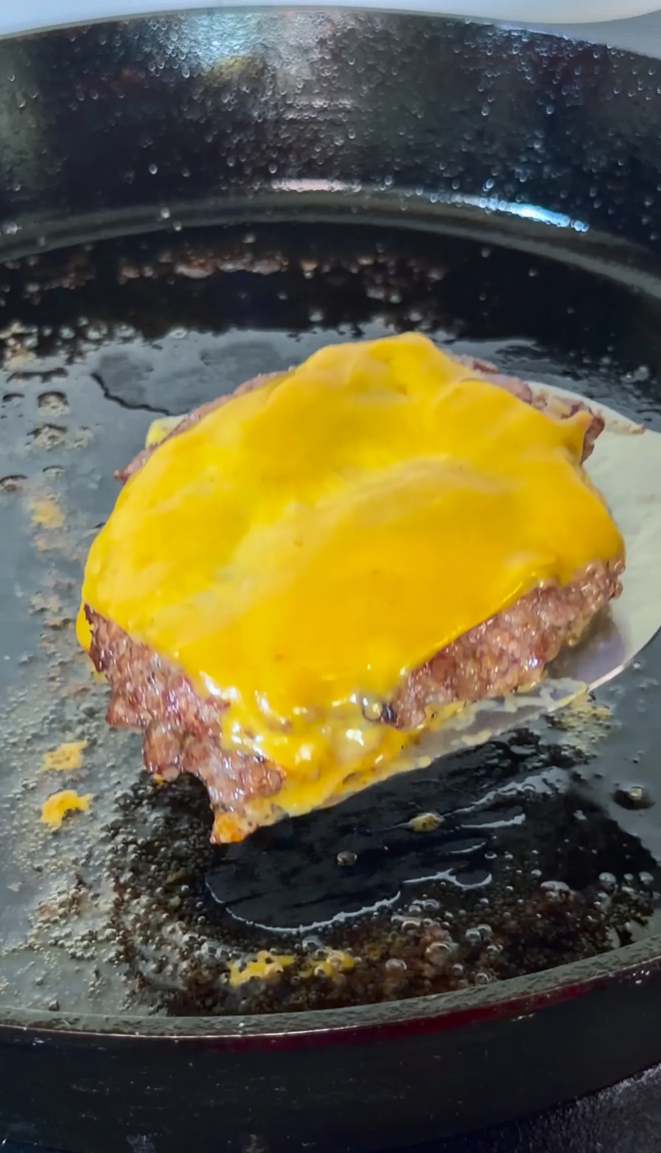 Bacon jam smash burger with melted cheese on a hot griddle showing caramelized edges