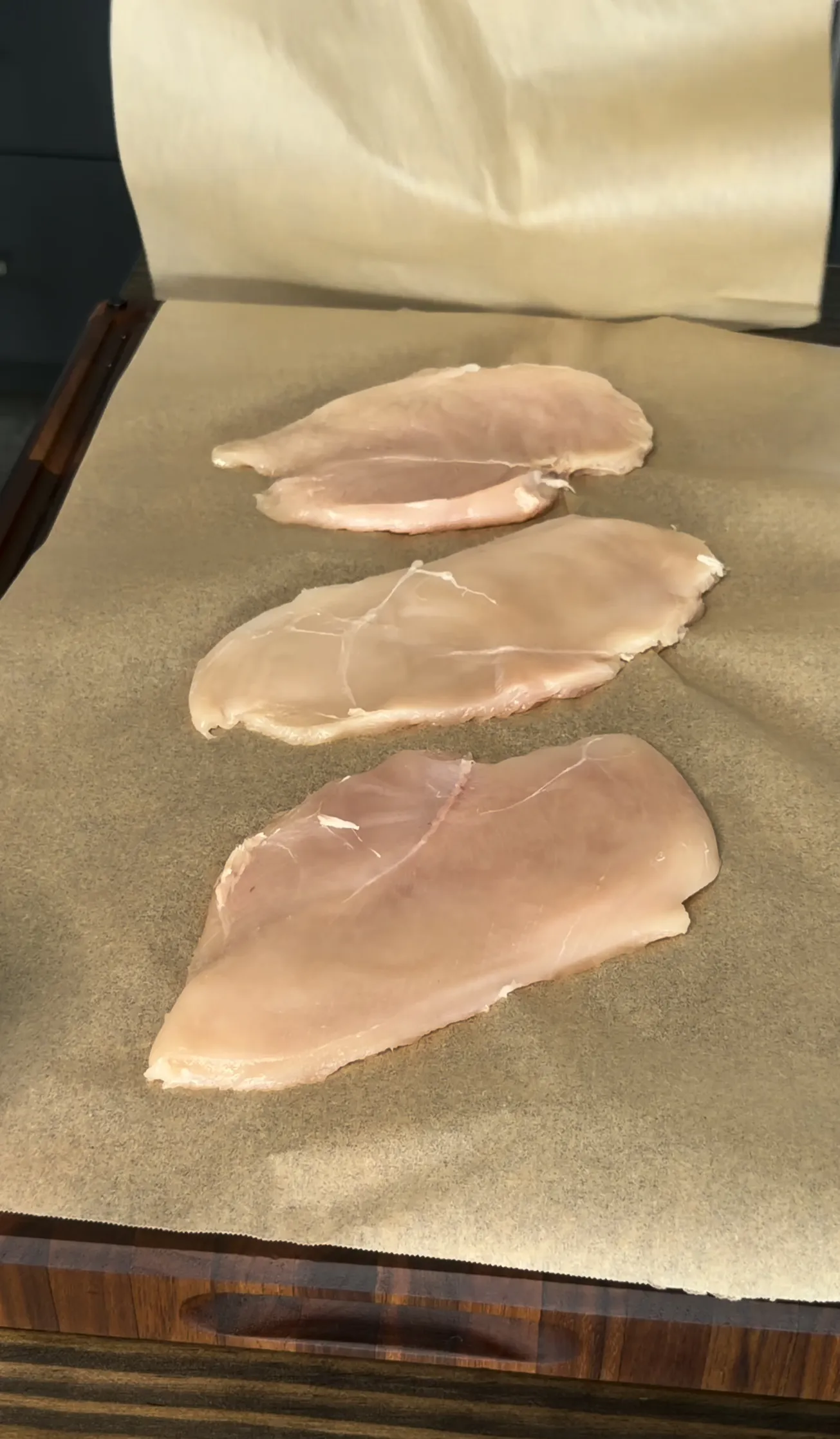 Raw chicken cutlets pounded flat on a cutting board
