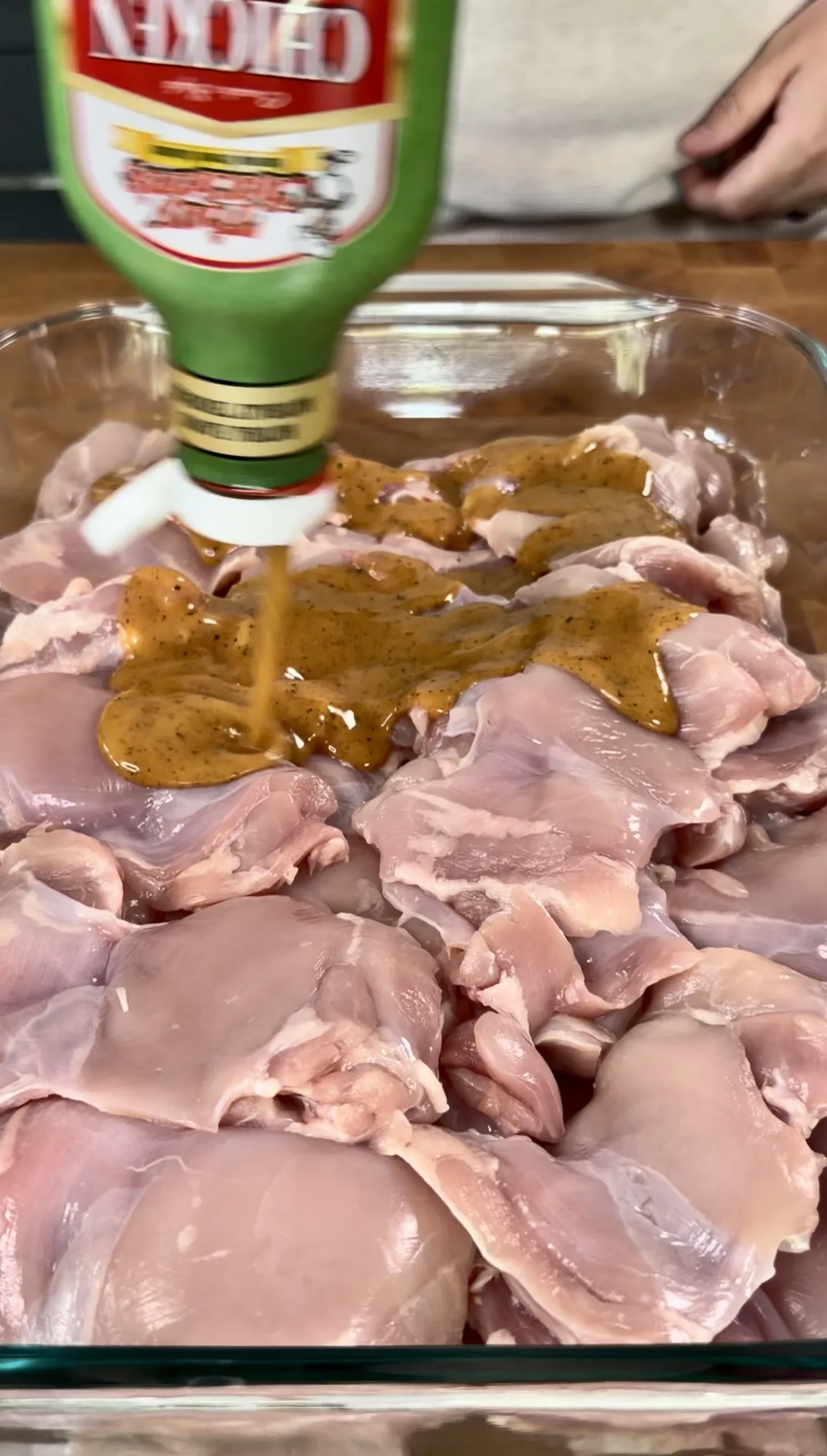 Raw chicken pieces marinating in olive oil and seasonings in a clear glass baking dish
