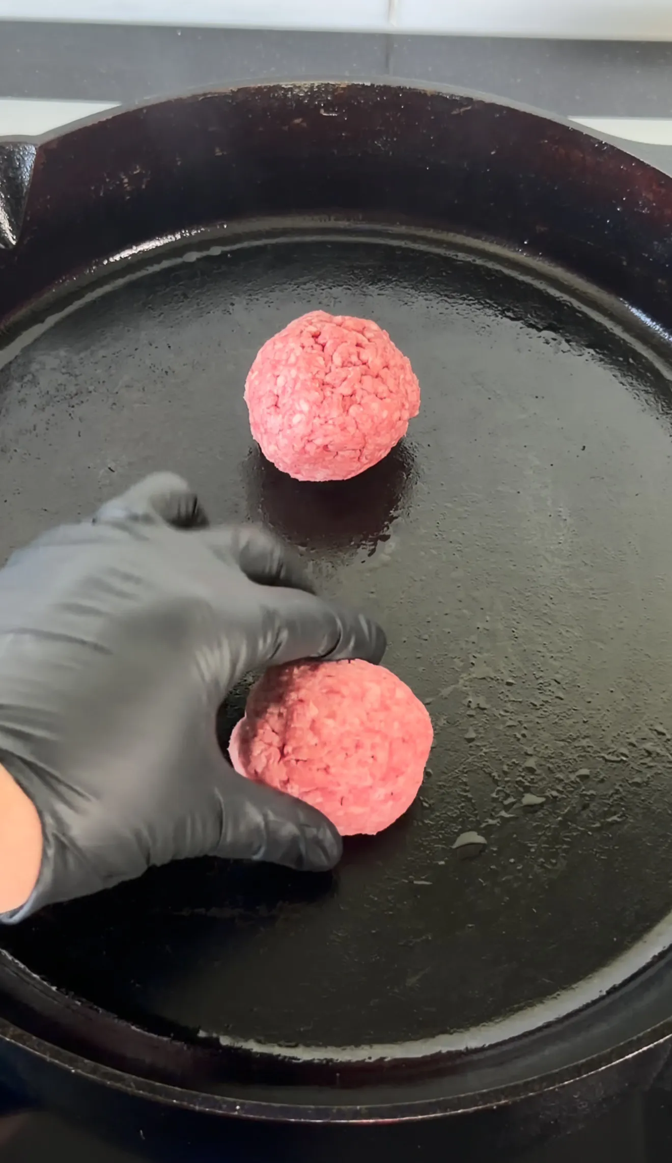 Raw ground beef patties being placed in a cast iron skillet for bacon jam smash burgers