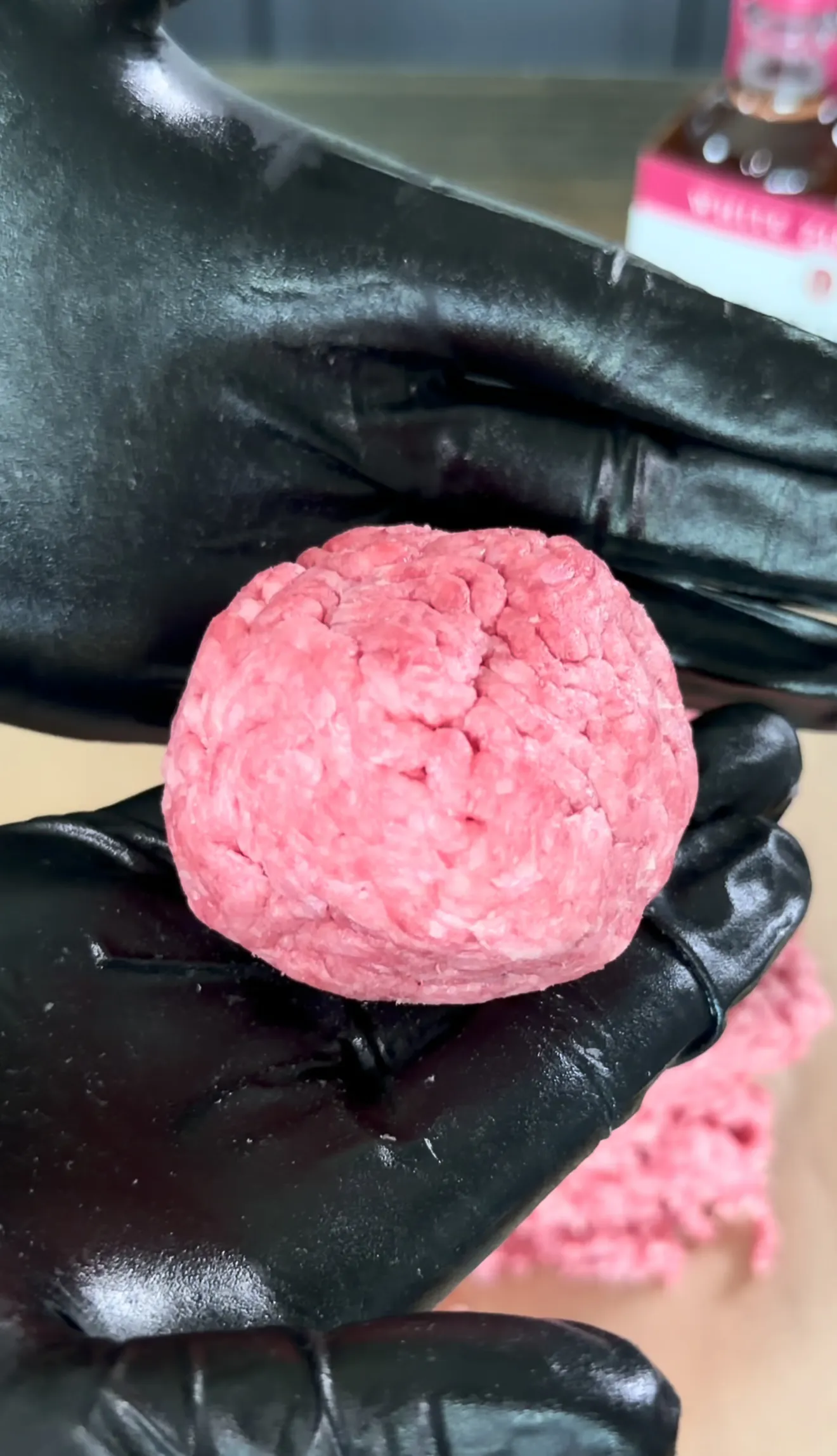 Raw ground beef patty held in black gloved hands for smash burger preparation