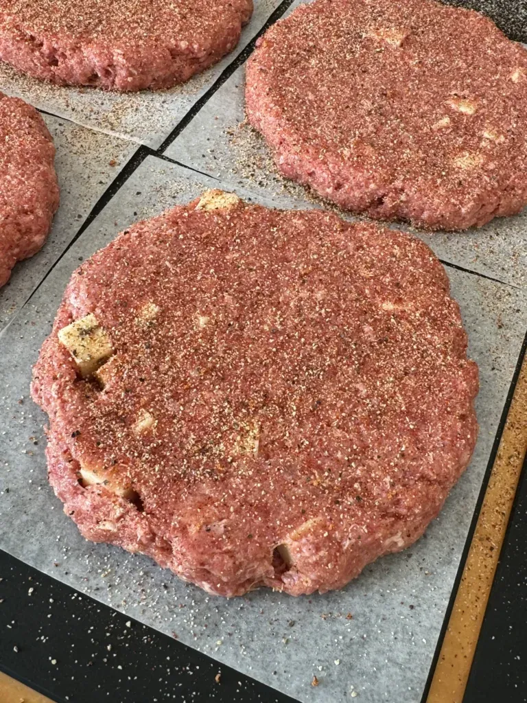 Raw seasoned Cajun burger patties on a cutting board ready for smoking