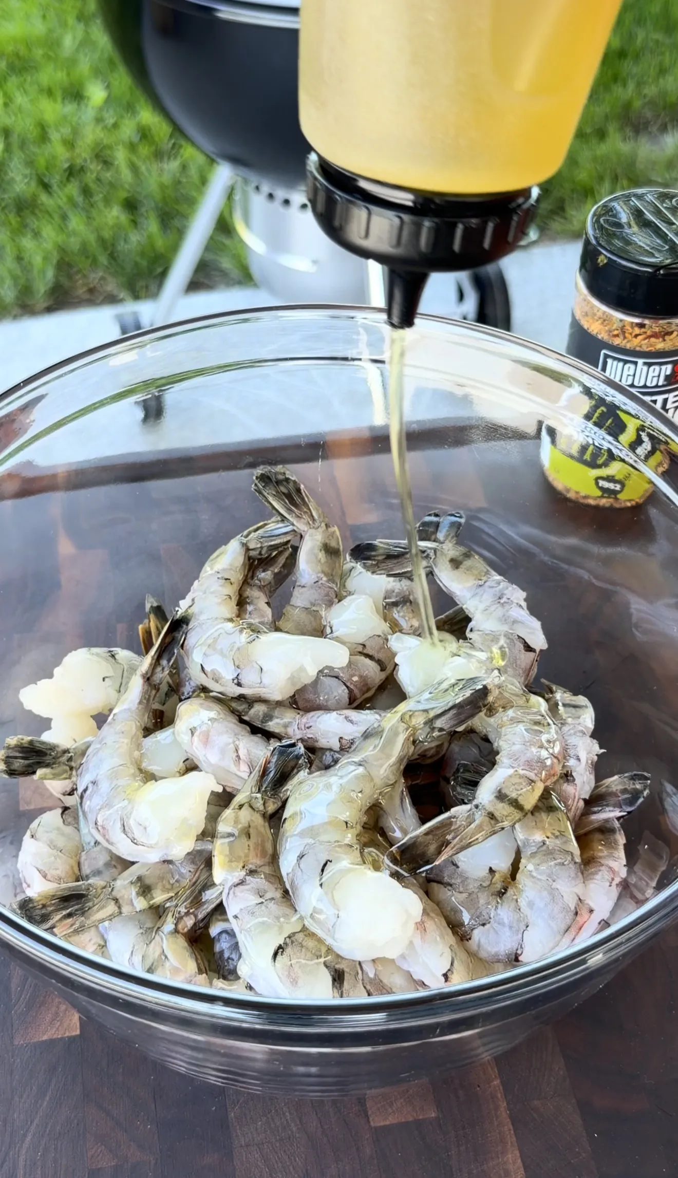 Raw shrimp in glass bowl being coated with avocado oil marinade for grilled skewers