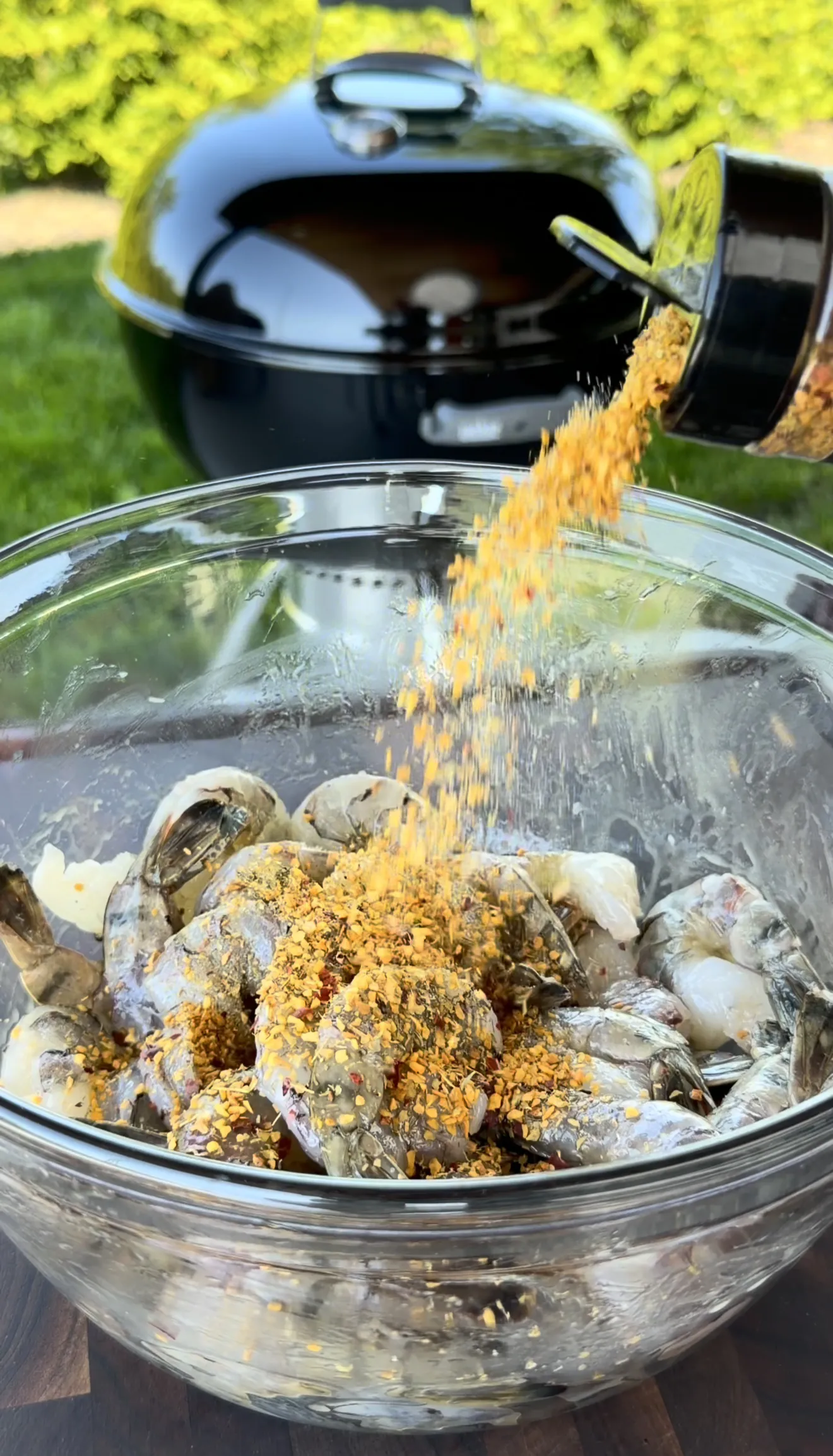 Raw shrimp in glass bowl being seasoned with roasted garlic herbs for grilled skewers