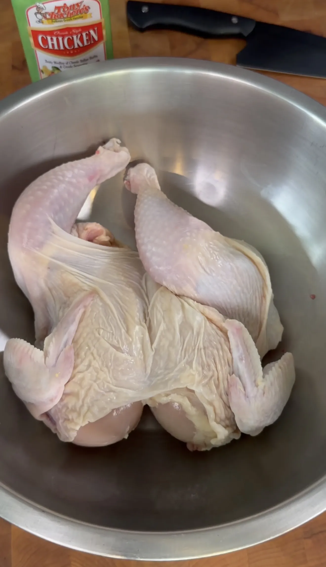 Raw whole chicken spatchcocked and flattened in a stainless steel bowl