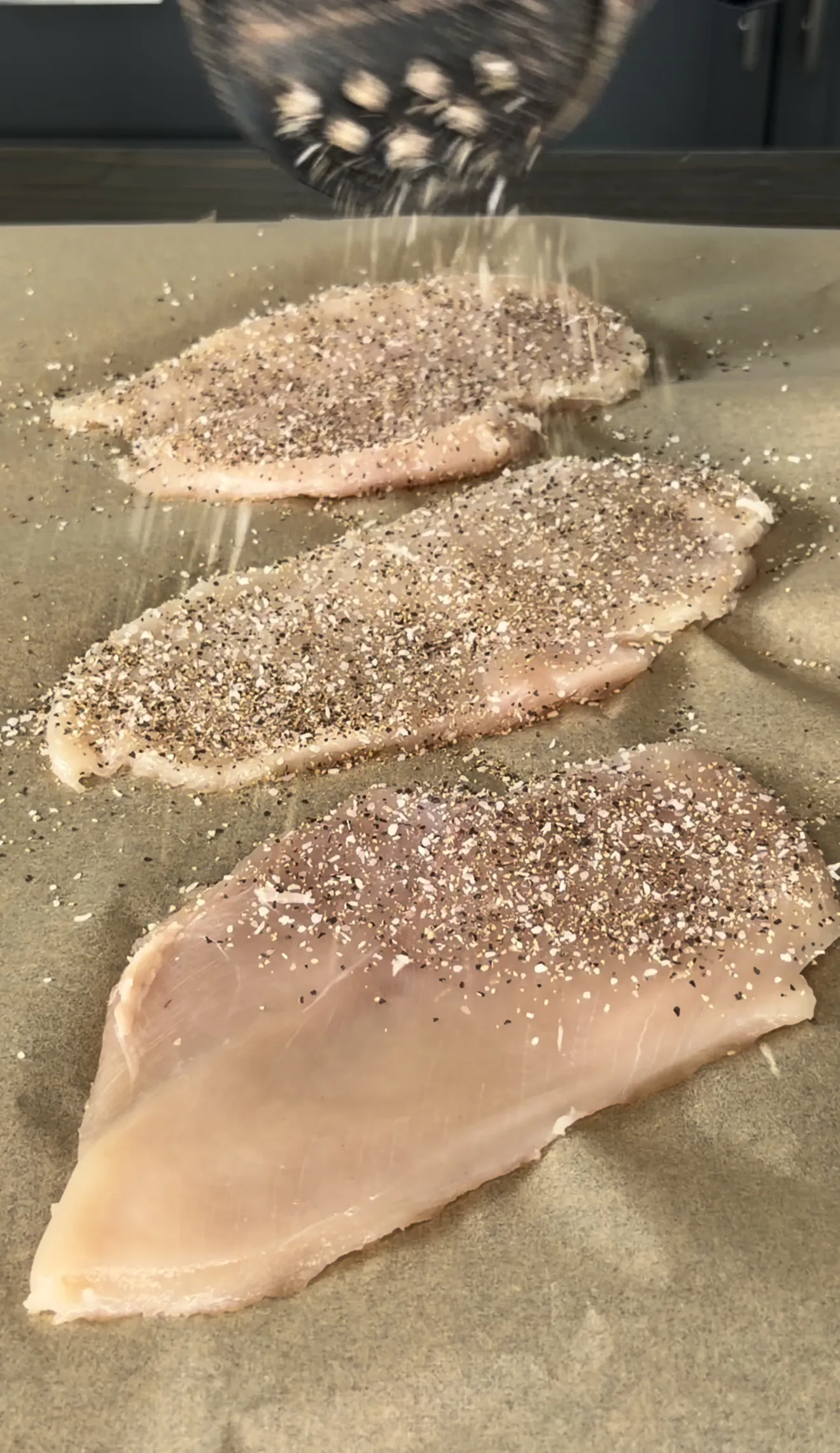 Seasoned chicken cutlets being prepared on a cutting board