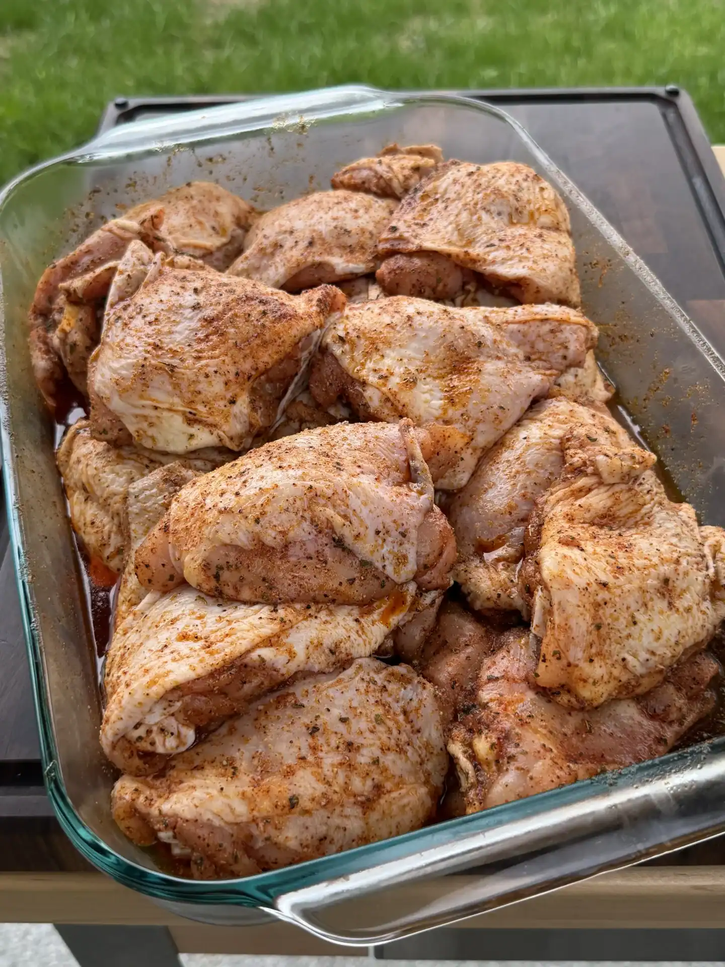 Raw chicken thighs seasoned with spices in a clear glass baking dish ready for cooking