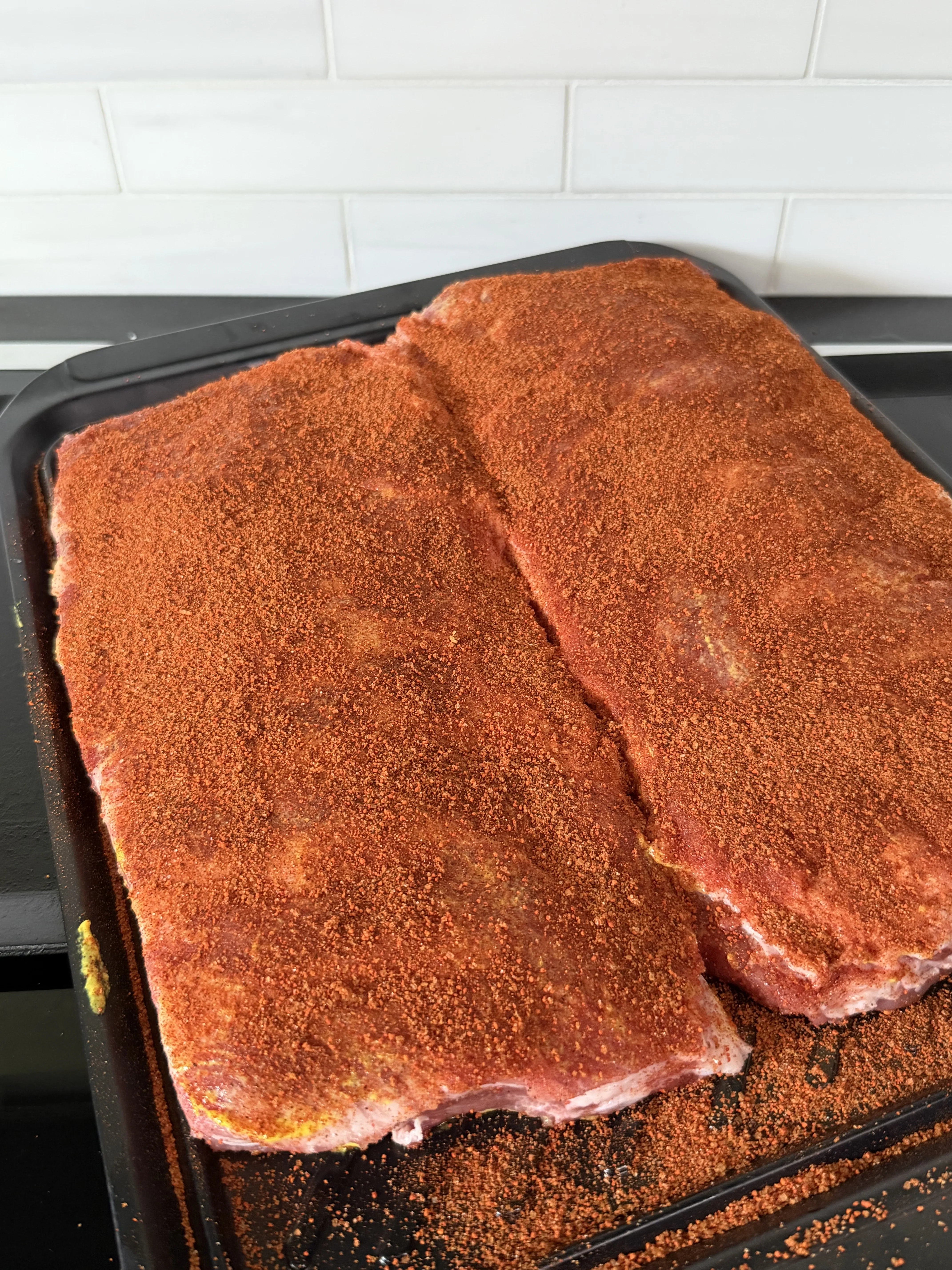Seasoned pork ribs with dry rub in a baking pan ready for the smoker