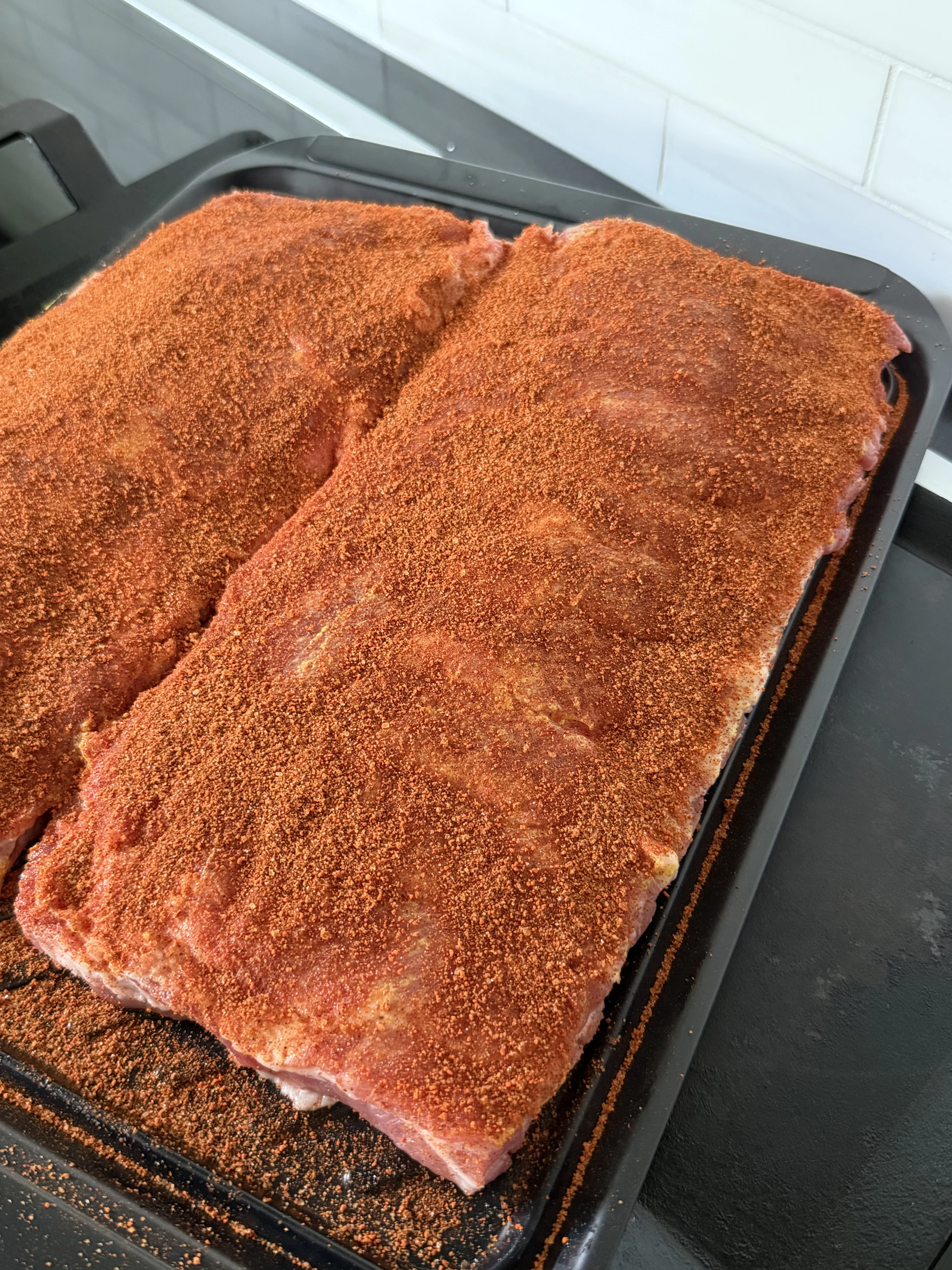 Seasoned pork ribs raw on a black tray ready for the pellet smoker