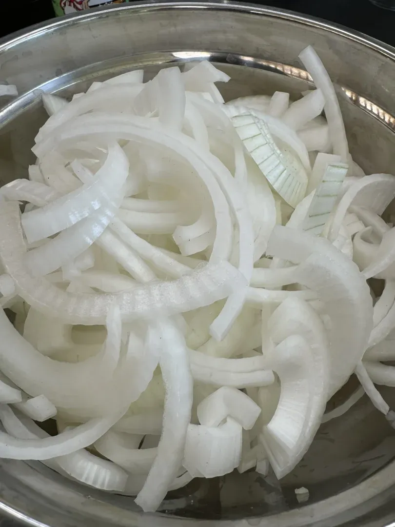 Freshly sliced white onions in a stainless steel mixing bowl for Cajun burger preparation