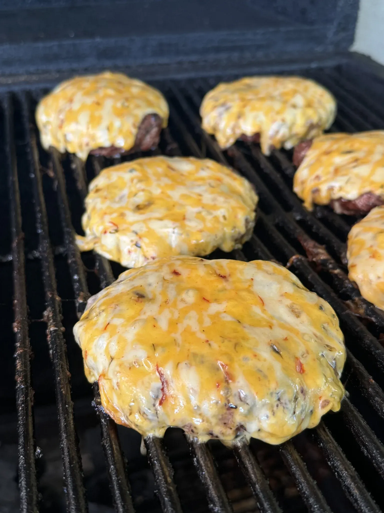 Smoked Cajun burgers topped with melted Colby jack 3-pepper cheese cooking on grill grates