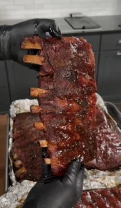 Glazed smoked pork ribs being held up showing caramelized bark and exposed bones